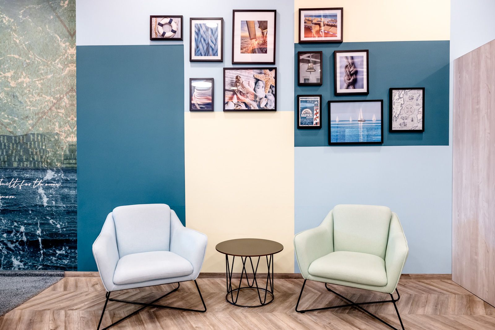 Gemütliche Sitzzone mit zwei modernen Sesseln in Pastellfarben, einem kleinen runden Tisch und einer Wand mit mehreren gerahmten Bildern, die eine entspannte Atmosphäre für Gäste schaffen.