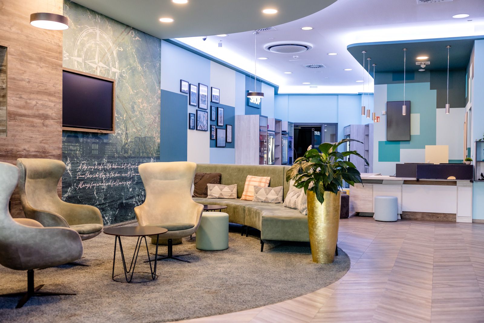 Moderner, einladender Hotellobby-Bereich mit stylischen Sesseln, Sofa, Teppich und Dekoration, heller Beleuchtung sowie Empfangstresen im Hintergrund. Angenehme Atmosphäre für Gäste zum Entspannen oder Warten.