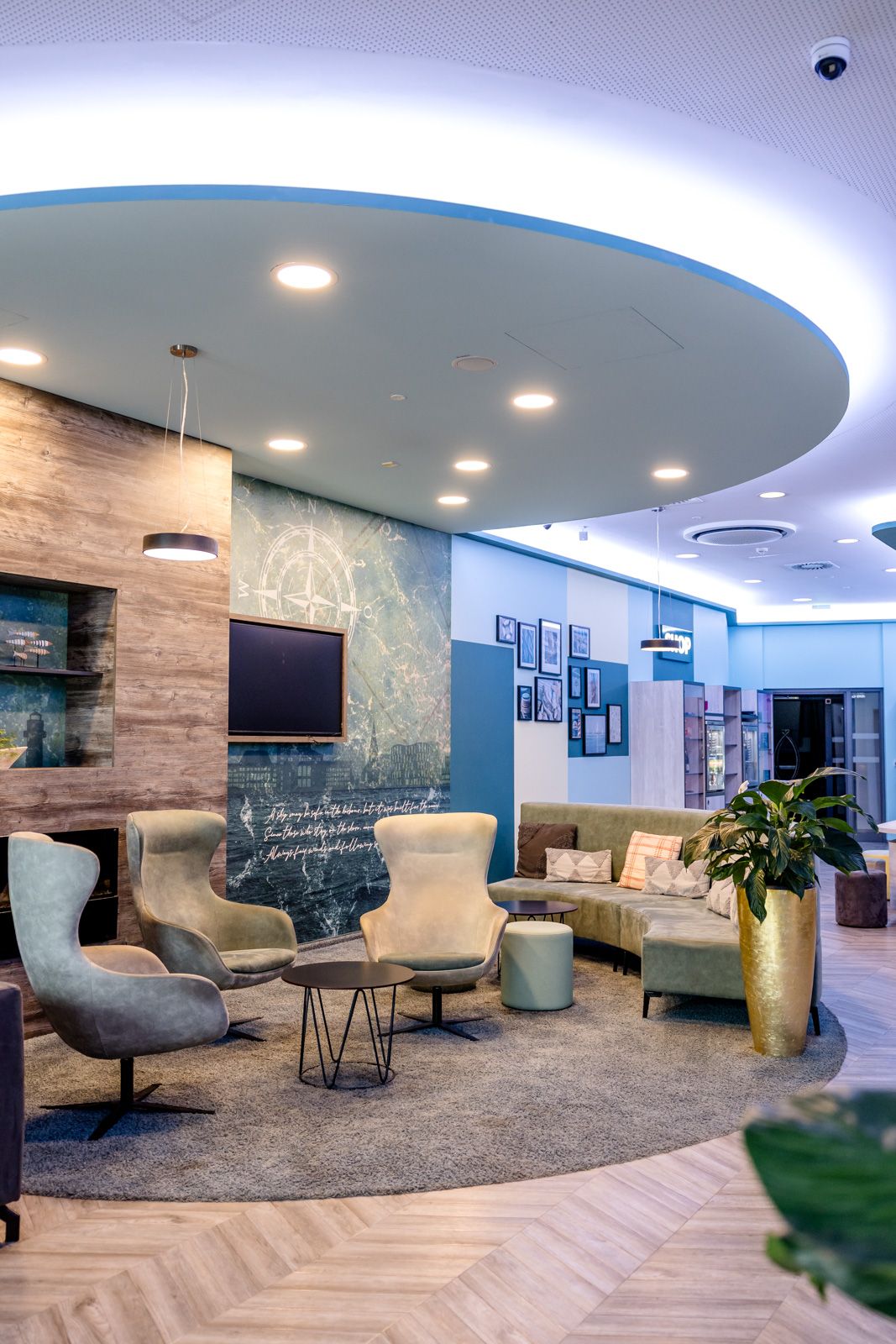 Moderne Lounge mit bequemen Sesseln und Sofas in warmem Ambiente, dekoriert mit Pflanzen und Kunst an den Wänden, ideal zum Entspannen oder für informelle Treffen.