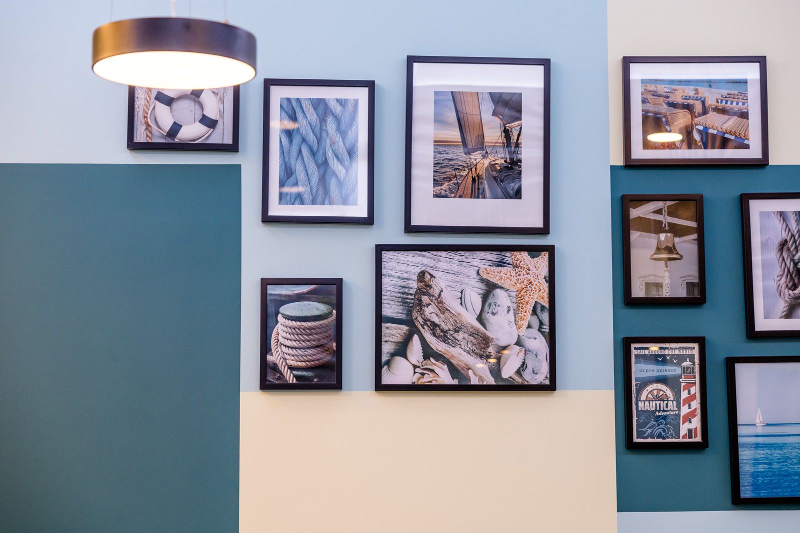 Mehrere maritime Bilder in schwarzen Rahmen an einer Wand, darunter Seile, ein Steuerrad, eine Seekarte, ein Leuchtturm und Strandmotive, erzeugen eine ruhige und nautische Atmosphäre.