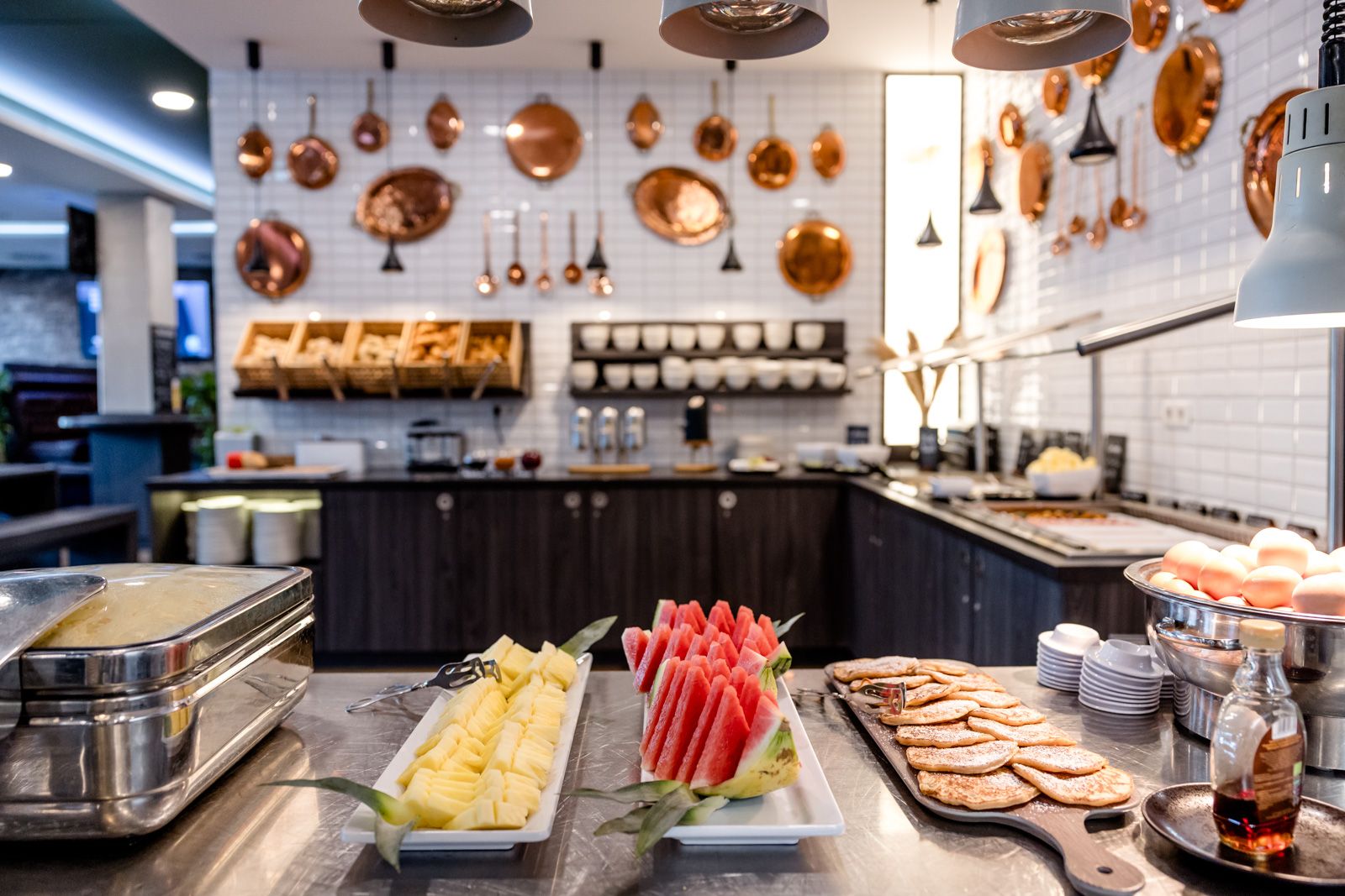 Buffet mit frischen Früchten wie Ananas und Wassermelone sowie Brot und anderen Speisen in moderner Hotelküche mit Kupfergeschirr dekoriert.