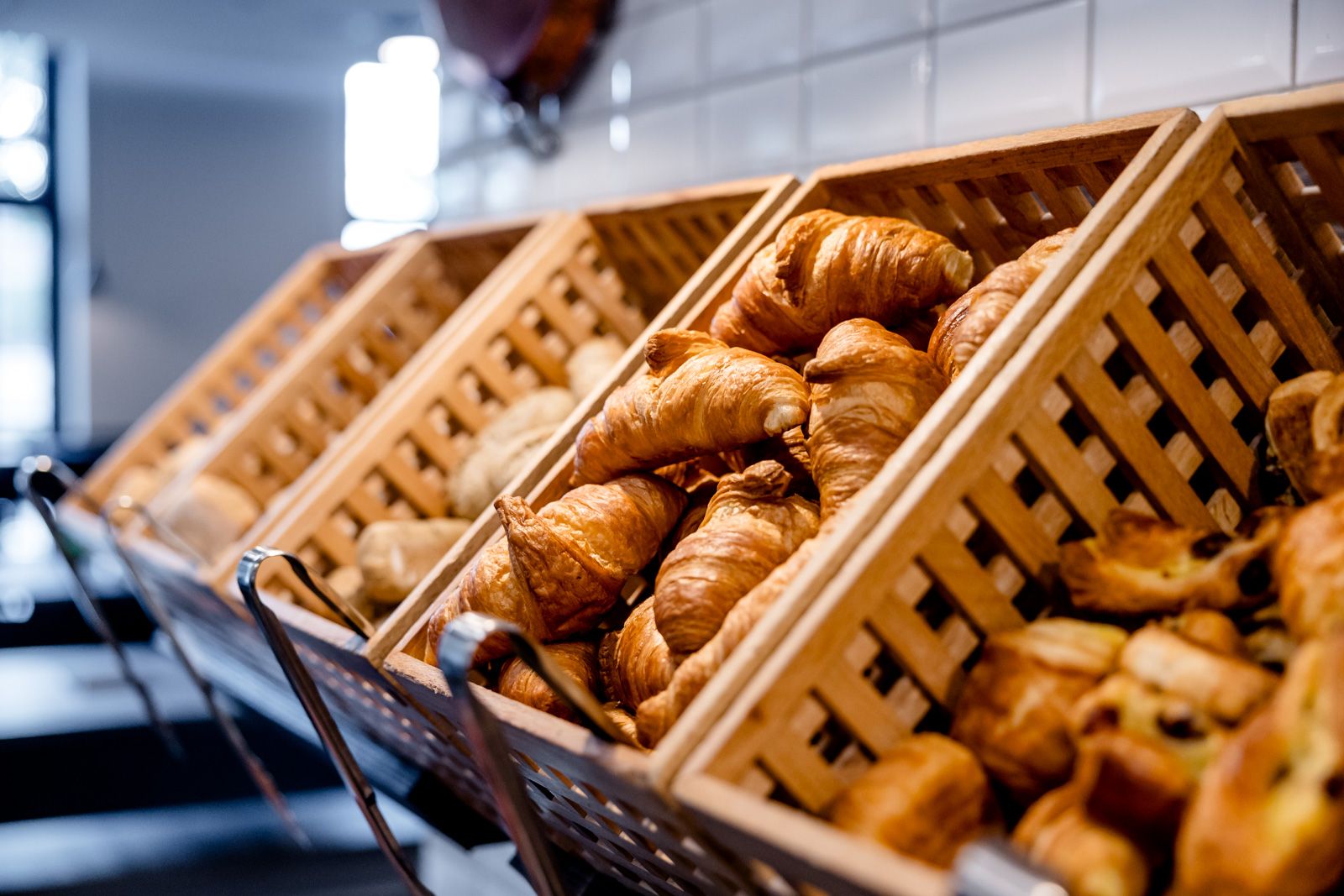 Verschiedene frische, goldbraun gebackene Croissants und Brötchen liegen in Holzkörben, bereit für ein großzügiges Frühstücksbuffet in einem Hotel.