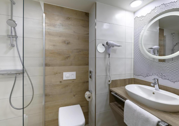 Modernes Badezimmer mit Dusche, Toilette und Waschbecken. Helle, freundliche Gestaltung mit Holz- und Fliesenelementen. Föhn und großer runder Spiegel sorgen für Komfort. Handtücher sind vorhanden, ideal für entspannte Erfrischung nach einem langen Tag.