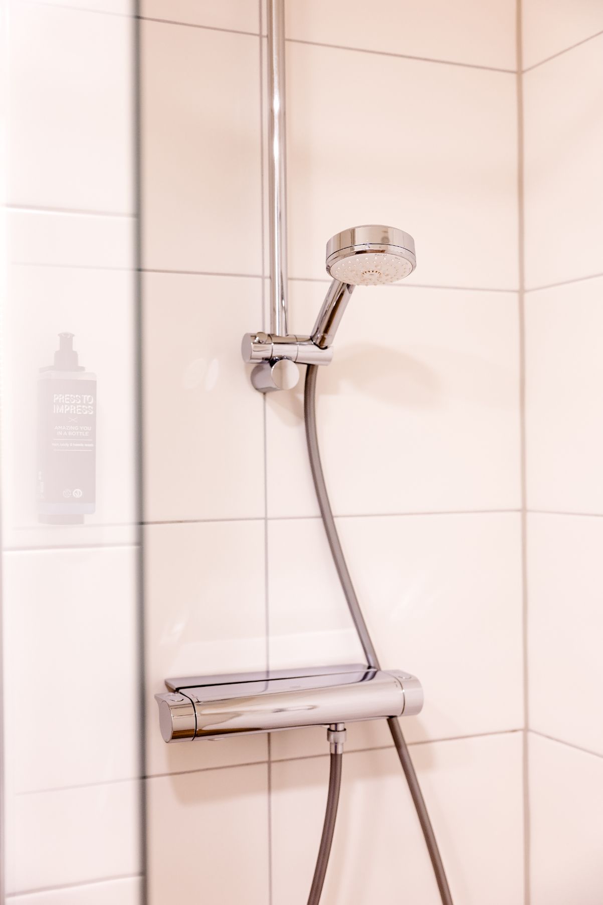 Moderne Duscharmatur mit verstellbarem Handbrausekopf und Thermostat in weiß gefliester Dusche, geeignet für entspannende und komfortable Duscherlebnisse im Hotelzimmer.