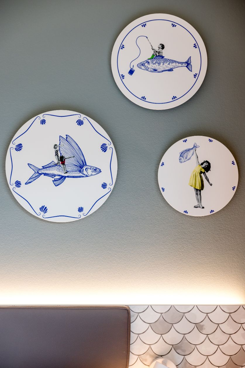 Drei dekorative Wandteller mit künstlerischen Darstellungen: Ein Kind auf einem fliegenden Fisch, ein Kind mit Angel auf einem Fisch und ein Kind, das einen Fisch am Schirm hält. Blaue Motive auf weißem Hintergrund, humorvoll und maritim gestaltet.