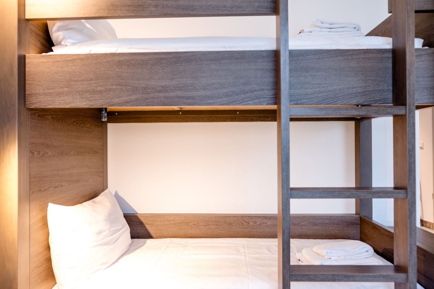 Zweistöckiges Etagenbett aus Holz mit weißer Bettwäsche und Kissen, Handtücher liegen ordentlich auf der unteren Liegefläche. Einfaches, funktionales Design für komfortables und platzsparendes Übernachten.