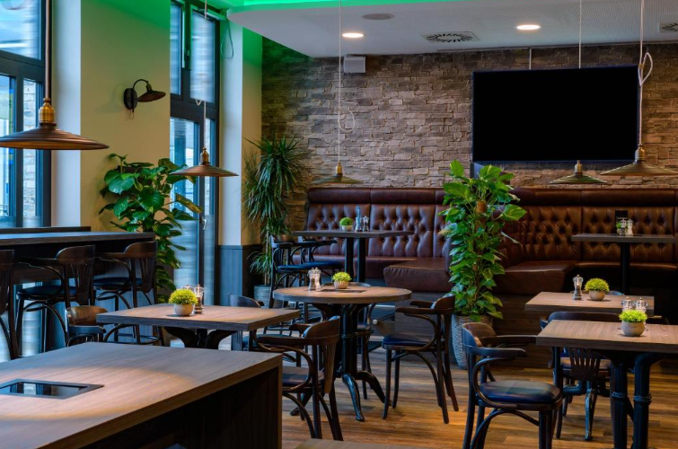 Modernes, gemütliches Restaurant mit Holztischen, gepolsterten Sitzbänken, grünen Pflanzen und indirekter Beleuchtung, das eine entspannte Atmosphäre für Gäste bietet.