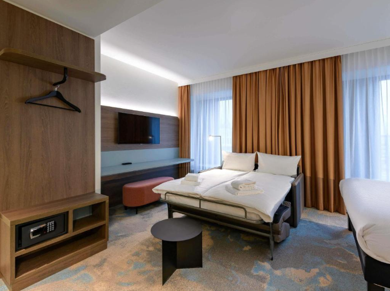 Modern eingerichtetes Hotelzimmer mit Doppelbett, TV, Panoramafenstern und warmen Vorhängen. Gemütliche Atmosphäre, ideal für Entspannung während Geschäfts- oder Urlaubsreisen.