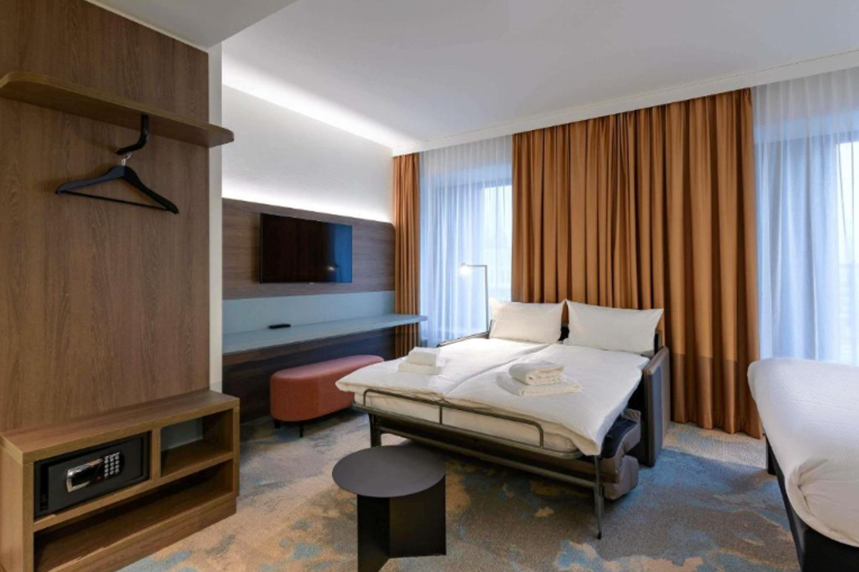 Modern eingerichtetes Hotelzimmer mit Doppelbett, TV, Panoramafenstern und warmen Vorhängen. Gemütliche Atmosphäre, ideal für Entspannung während Geschäfts- oder Urlaubsreisen.
