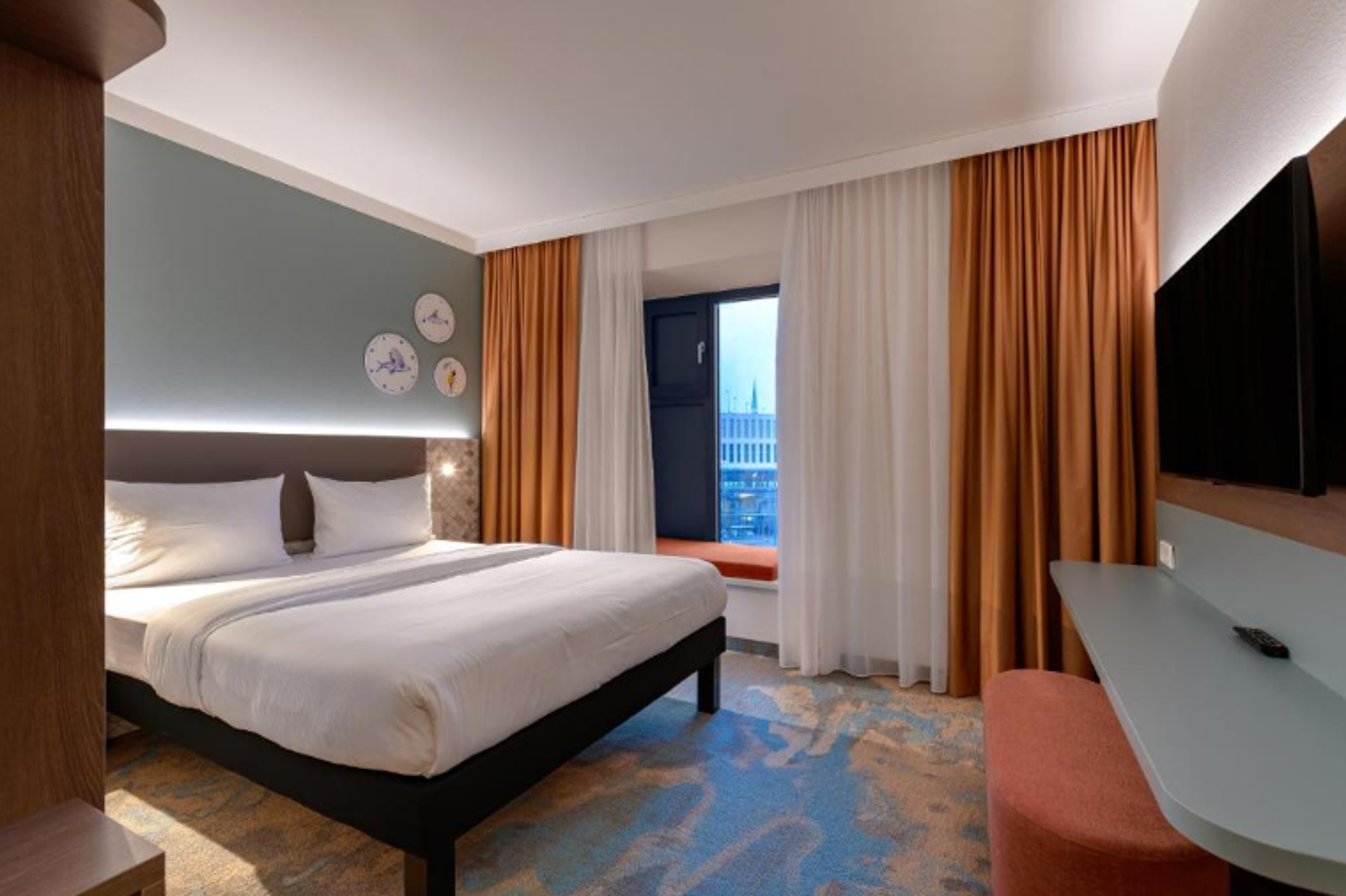 Modern eingerichtetes Hotelzimmer mit großem Doppelbett, beruhigenden Farbtönen, Blick durch Fenster auf Stadt und bequemer Sitzgelegenheit. Ruhige, einladende Atmosphäre für erholsamen Aufenthalt. Modern eingerichtetes Hotelzimmer mit großem Doppelbett, beruhigenden Farbtönen, Blick durch Fenster auf Stadt und bequemer Sitzgelegenheit. Ruhige, einladende Atmosphäre für erholsamen Aufenthalt.