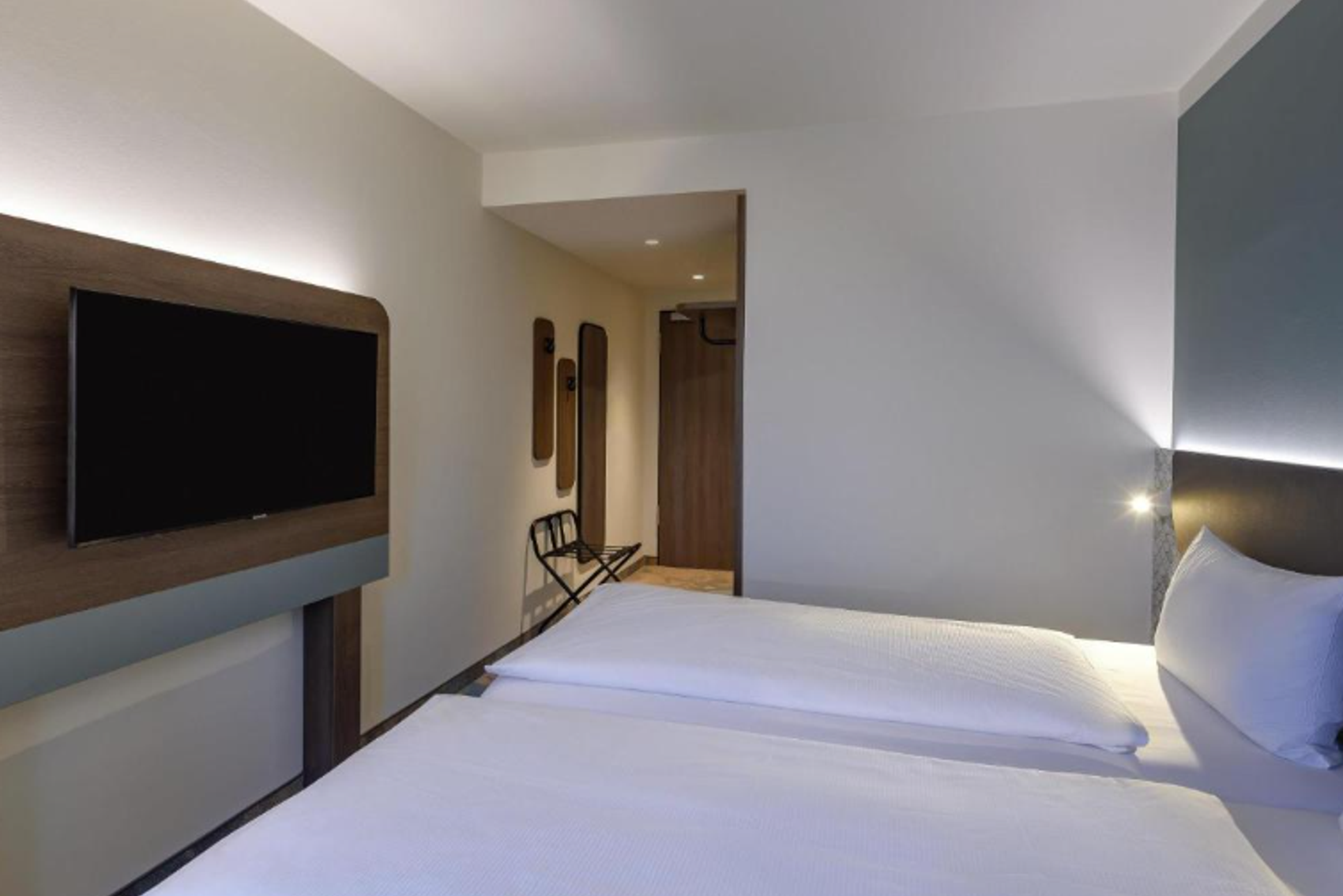 Modern eingerichtetes Hotelzimmer mit großem Bett, hellem Ambiente und Flachbildfernseher an der Wand, ideal für erholsamen Aufenthalt.