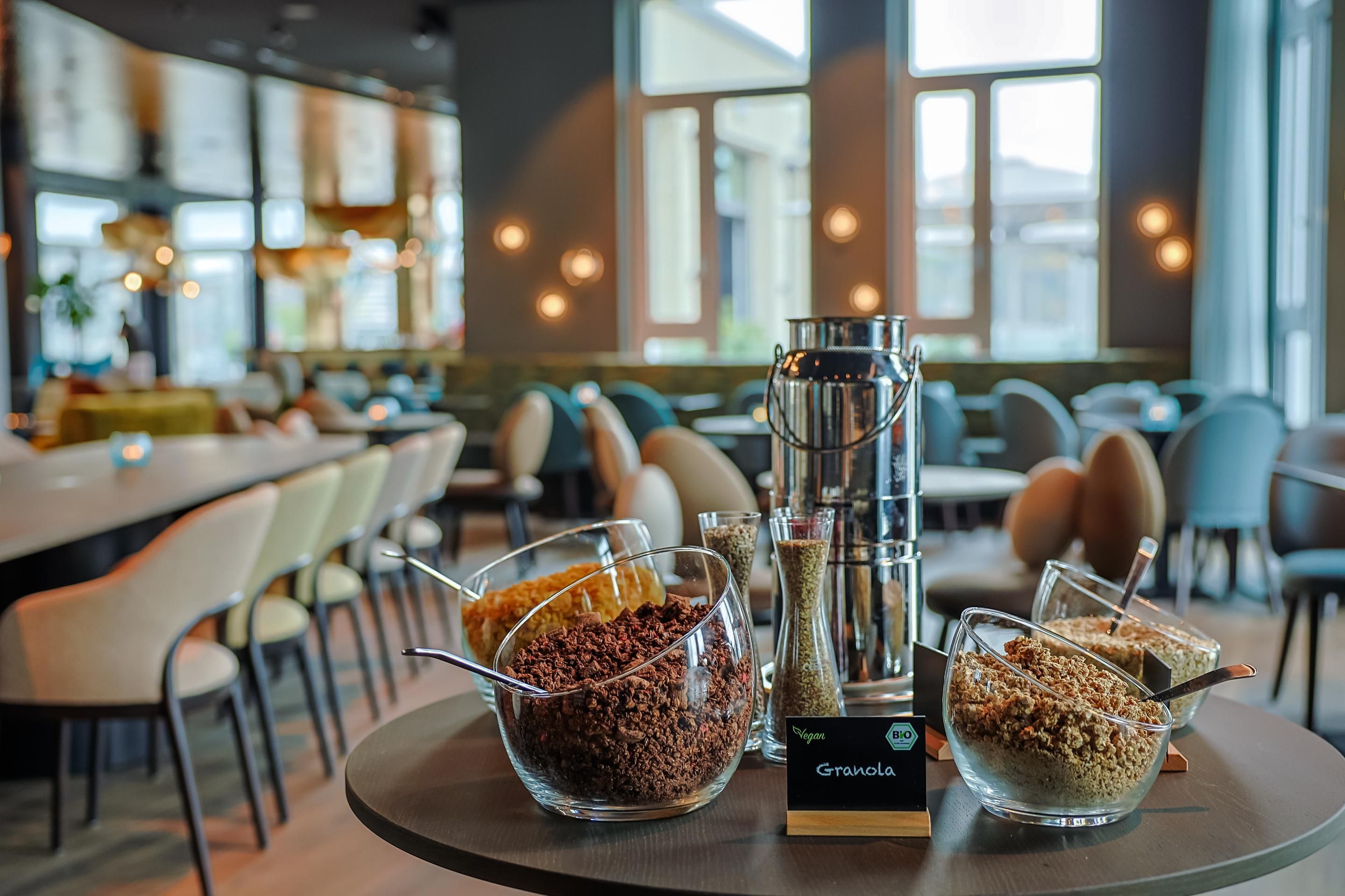 Frühstücksbuffet mit mehreren Schalen Granola in einem modernen, hellen Restaurant mit großen Fenstern und stilvoller Einrichtung.