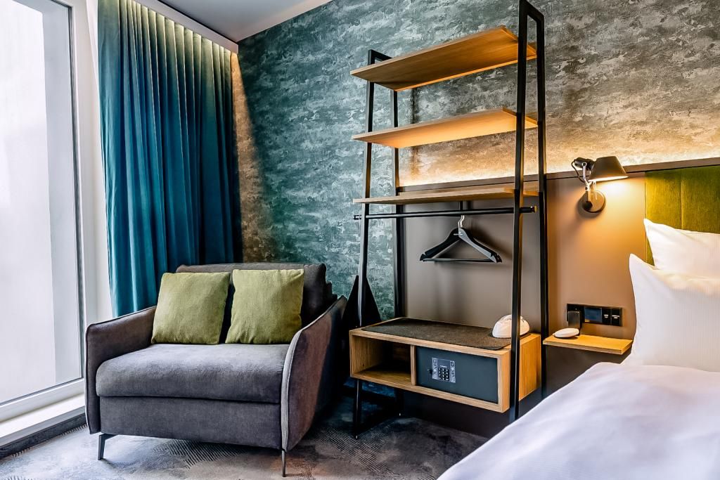 Gemütliche Hotelsuite mit modernem Sessel, weichen Kissen, offenem Kleiderregal und sanfter Beleuchtung, die eine einladende Atmosphäre zum Entspannen schafft.