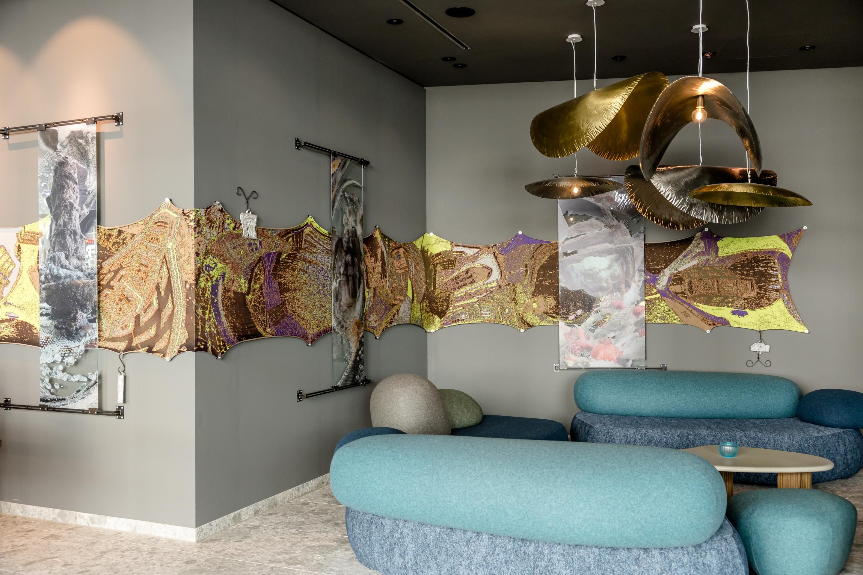 Moderner Lounge-Bereich mit geschwungenen, blauen Sofas und künstlerischer Wanddekoration aus textilen Elementen und Metallskulpturen, die dem Raum eine elegante und kreative Atmosphäre verleihen.