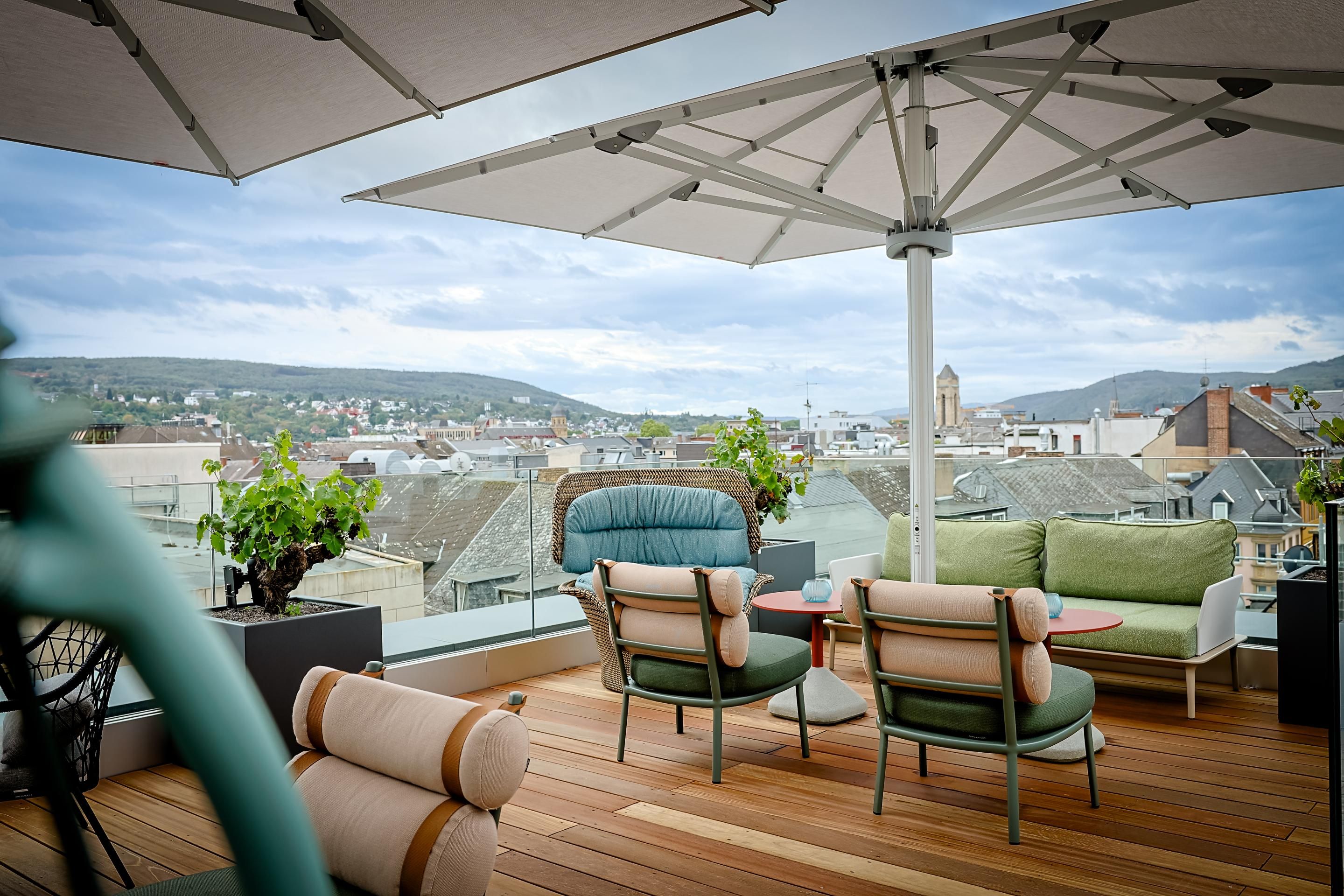Dachterrasse mit gemütlichen Sitzmöbeln und Sonnenschirmen, Blick auf Stadt und grüne Hügel im Hintergrund, einladender Platz zum Entspannen und Genießen.