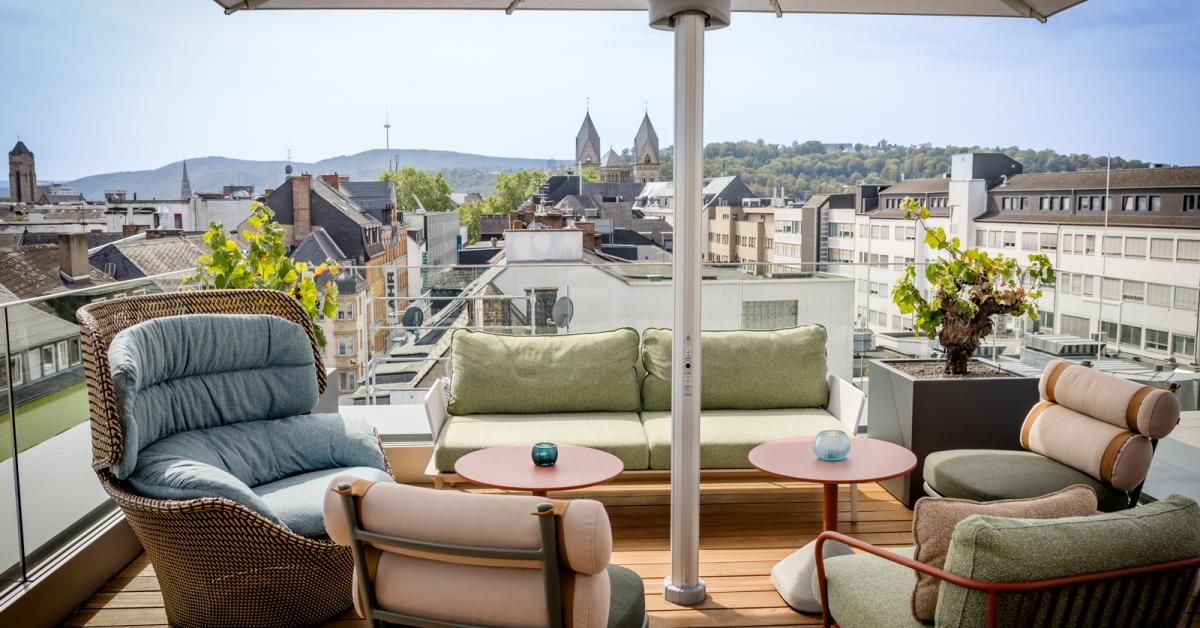 Gemütliche Dachterrasse mit gepolsterten Sesseln und Sofa, kleine Tische und Blick auf die Stadt und umliegende Hügel, ideal für Entspannung und Geselligkeit.