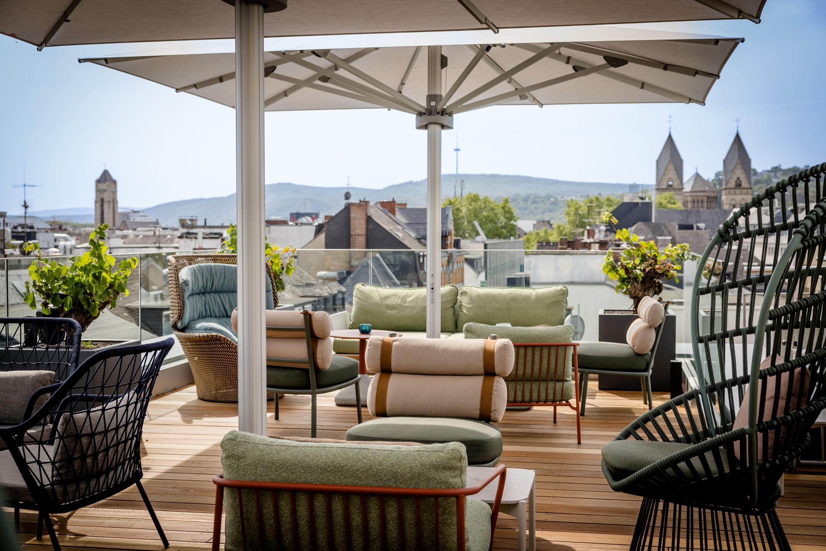 Dachterrasse mit gemütlichen Sitzmöbeln und großen Sonnenschirmen, bietet entspannte Atmosphäre und Ausblick auf historische Stadtgebäude und Hügel im Hintergrund.