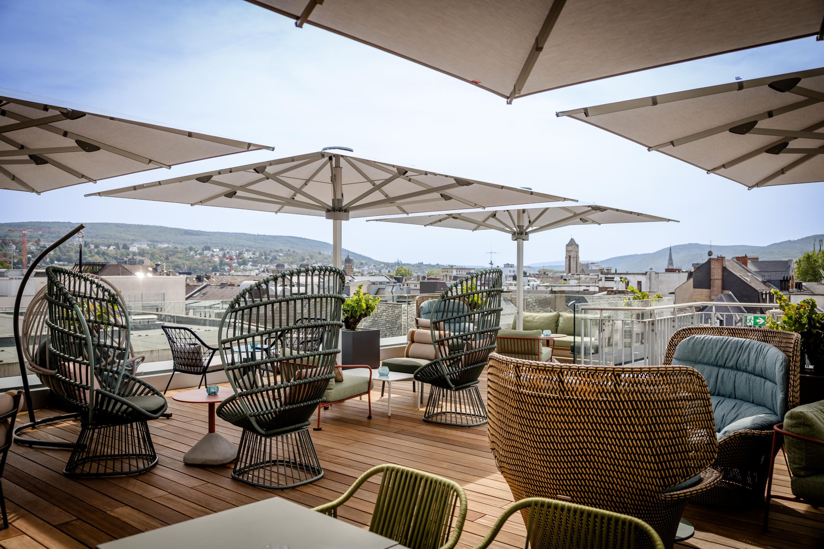 Dachterrasse mit komfortablen Sitzgelegenheiten, großen Sonnenschirmen und Blick über die Stadt bis zu den Bergen, ideal zum Entspannen und Genießen der Aussicht.