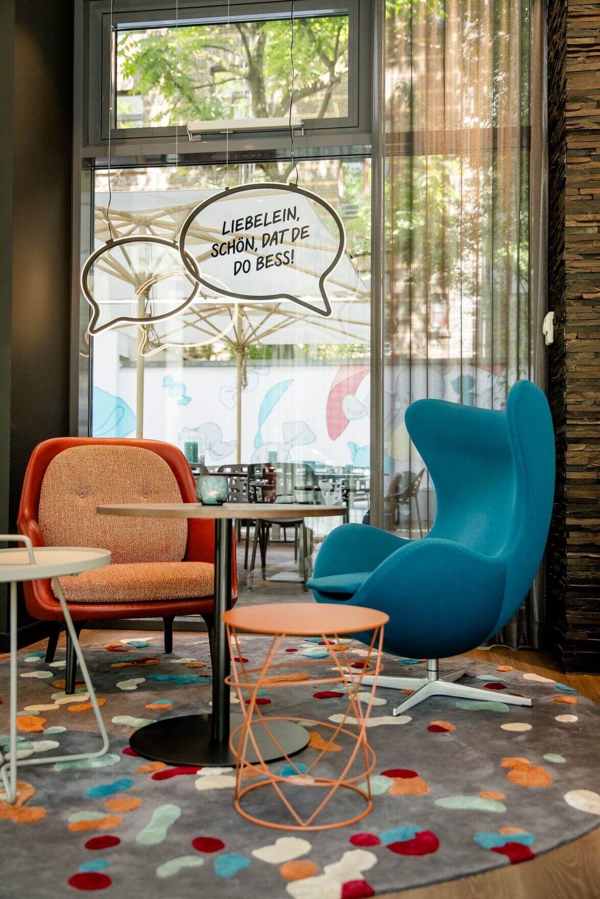 Designhotel Köln Mediapark Motel One zwei Sessel vor großer Glasscheibe mit Dekoration in Form von Sprechblasen