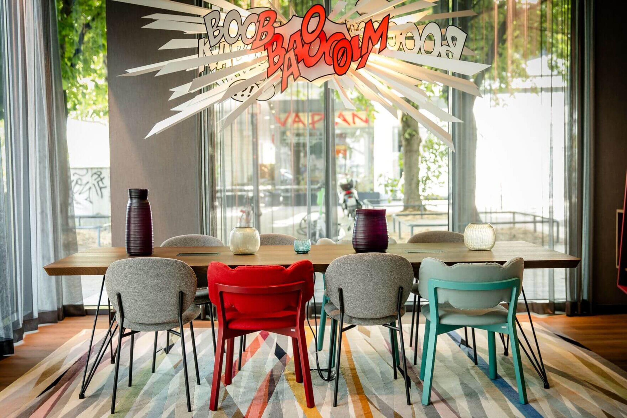 Designhotel Köln Mediapark Motel One lichtdurchfluteter Meetingraum mit Tisch, acht Stühlen und dekorativer Comic-Lampe