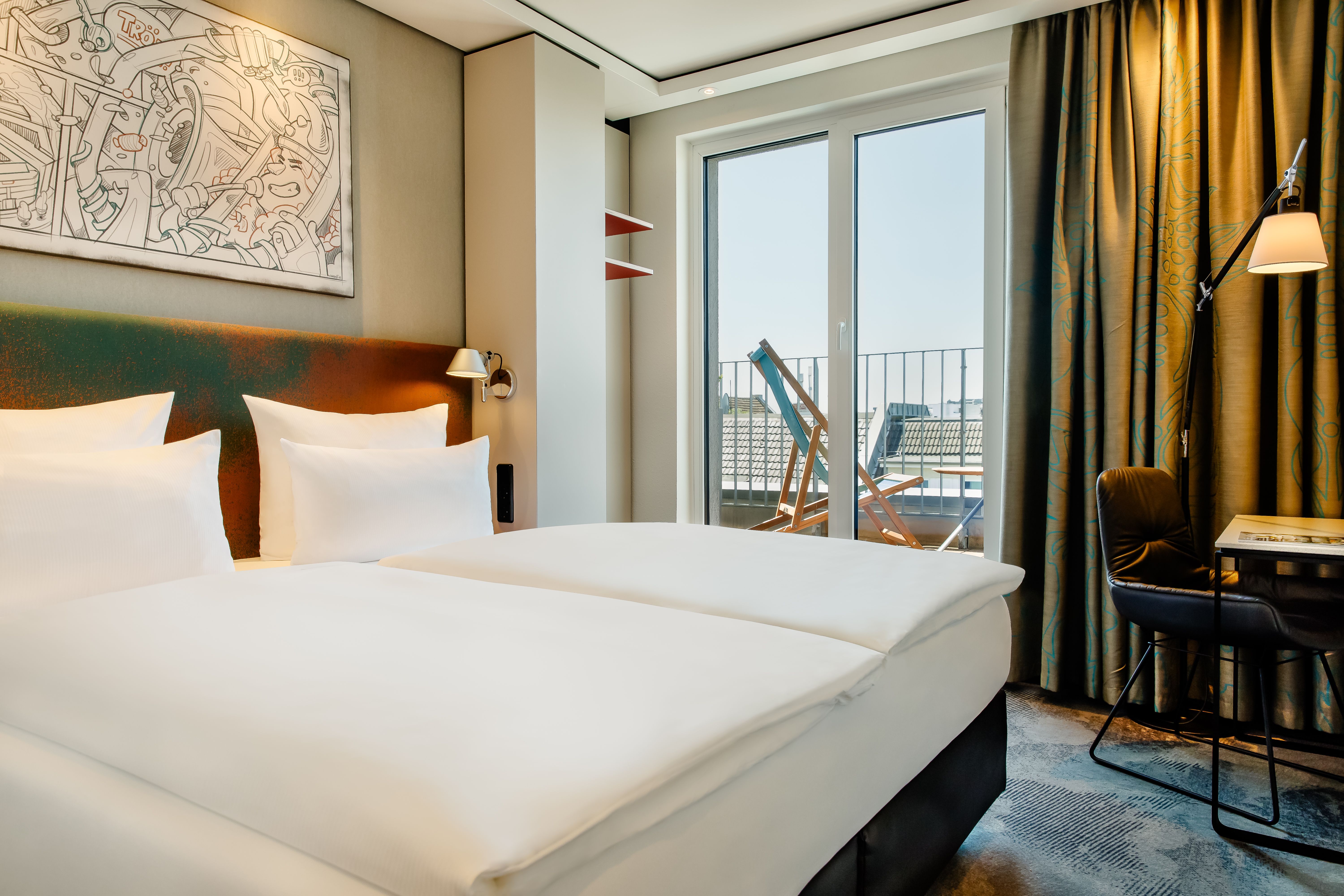 Designhotel Köln Mediapark Motel One lichtdurchflutetes Zimmer mit Bett, Schreibtisch, Sessel sowie bodentiefem Fenster