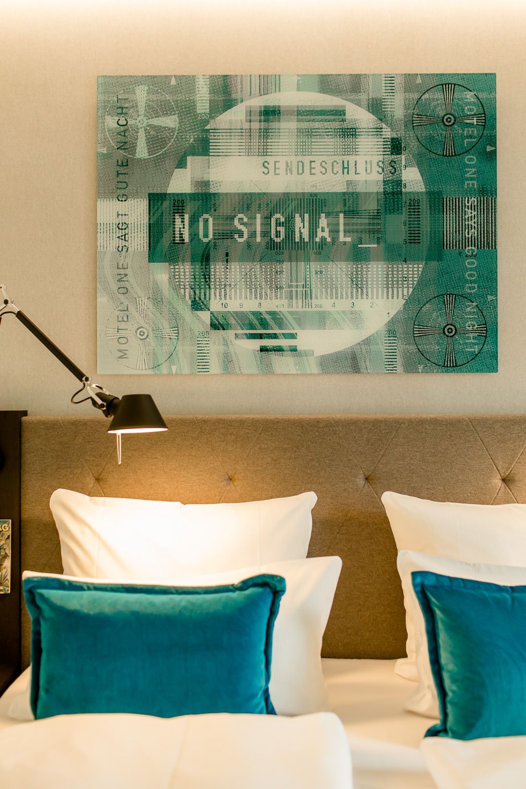 Hotel Köln Messe Motel One Blick auf Kopfteil eines Doppelbettes sowie Zierkissen und Bild über dem Bett