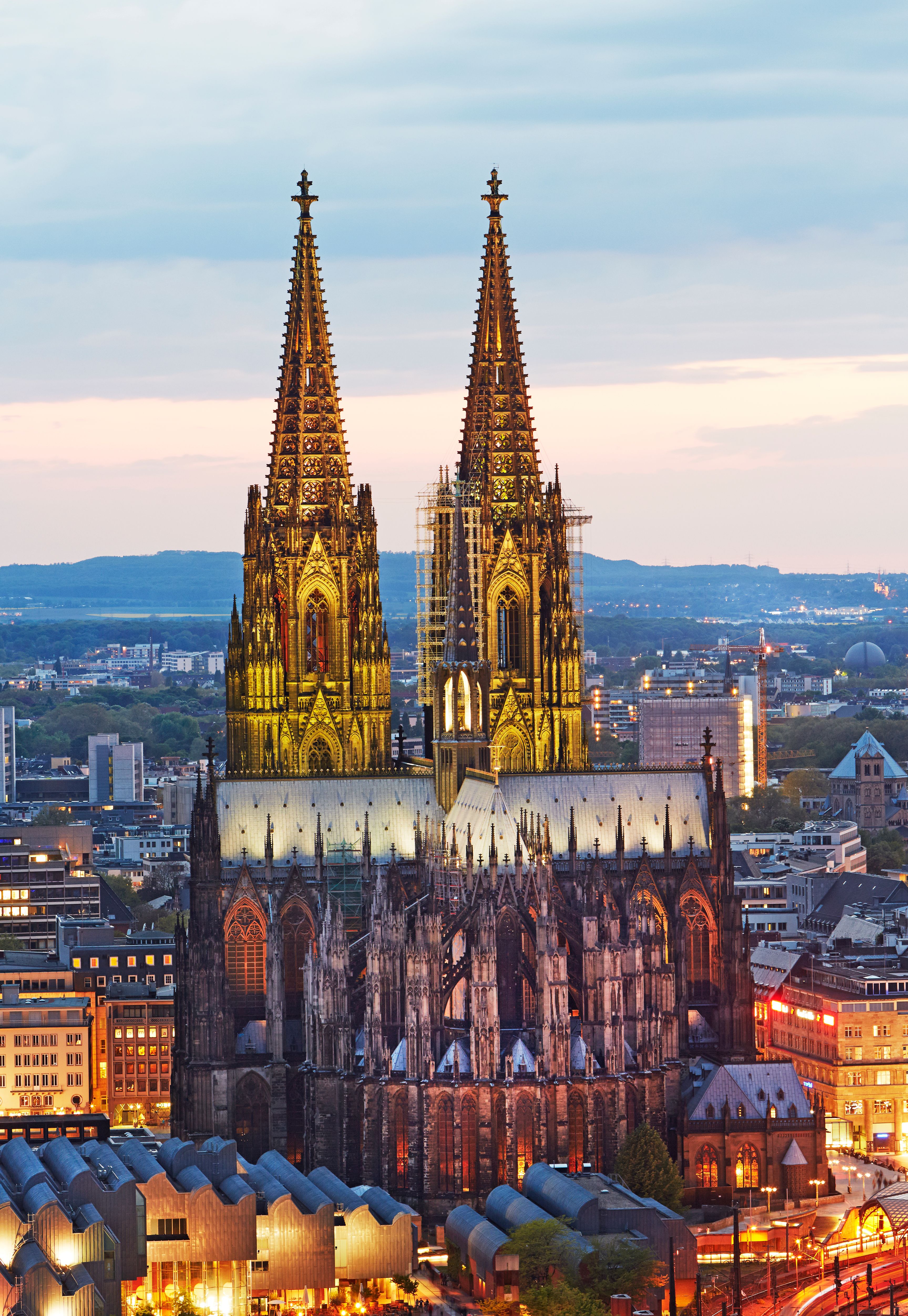 Beeindruckender Blick auf den beleuchteten Kölner Dom bei Abenddämmerung, umgeben von der modernen Stadtlandschaft Kölns.