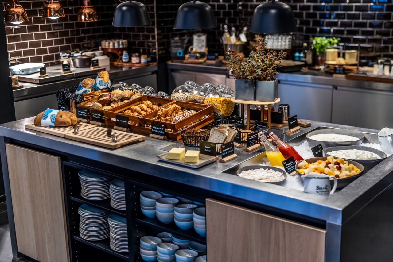 Frisches Frühstücksbuffet mit verschiedenen Brotsorten, Croissants, Müsli, Joghurt, frischem Obst und Säften in modernem, einladendem Ambiente.