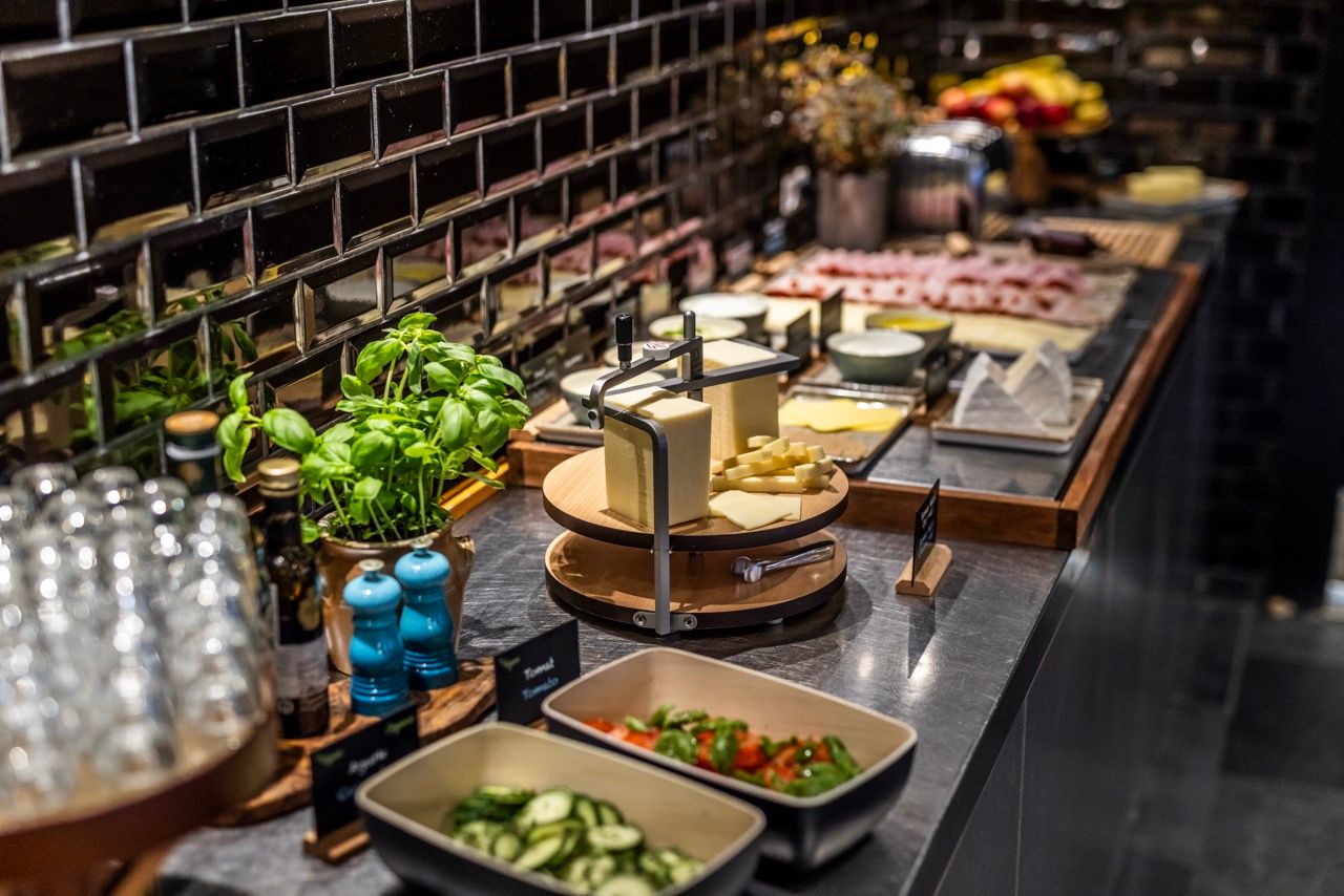Buffet mit frischen Salaten, Käsevariationen, Aufschnitt, Kräutern und Gewürzen, ansprechend angerichtet auf einer modernen Theke in warmem Licht.