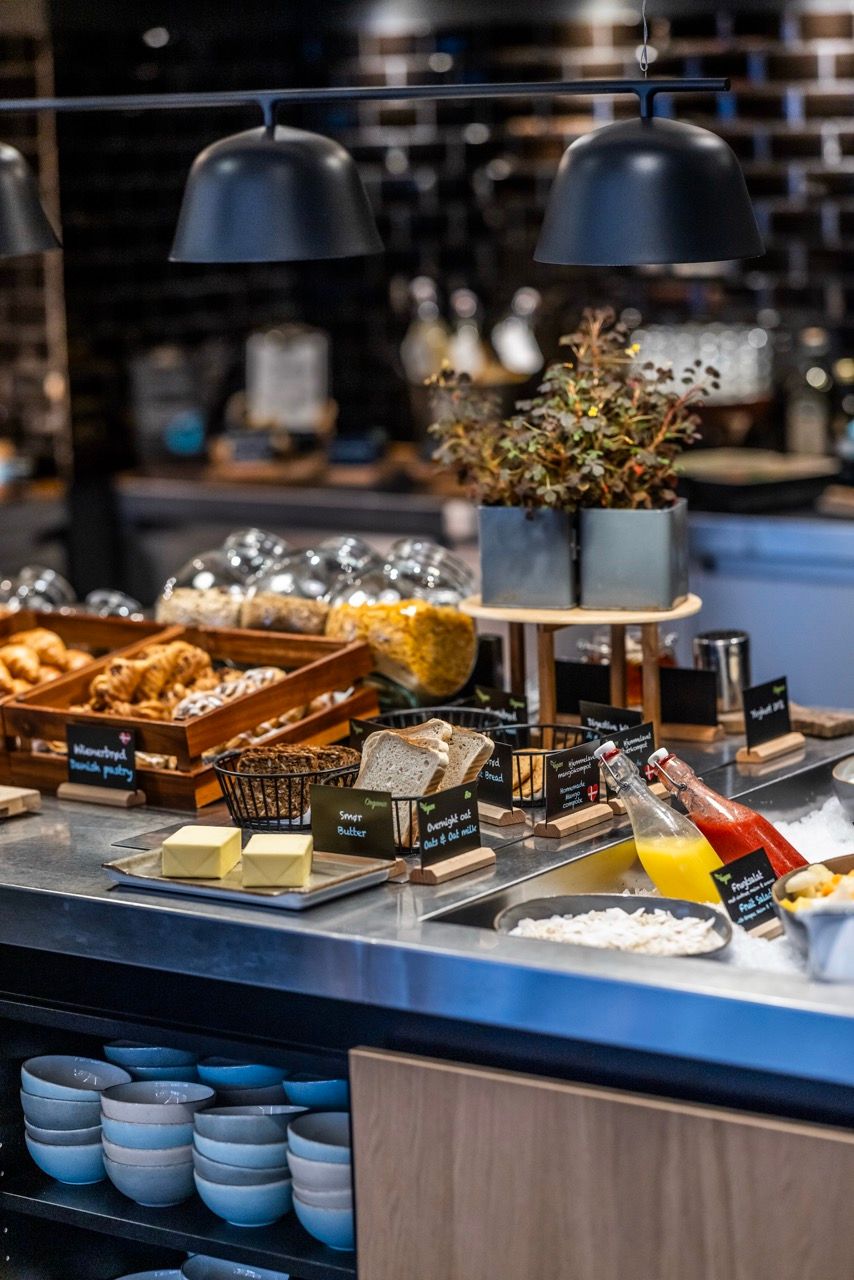 Buffet mit vielfältigem Frühstücksangebot, darunter frisches Gebäck, Brot, Butter, Müsli, Säfte und Joghurt, ansprechend und einladend präsentiert in modernem Ambiente.