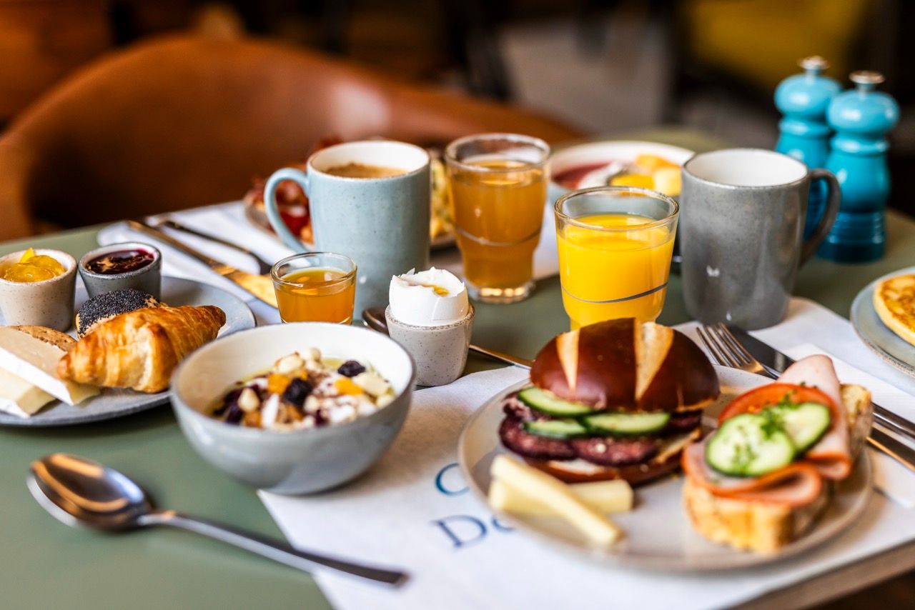 Frühstückstisch mit frischem Croissant, Müsli, Sandwiches, Orangensaft, Kaffee und Marmelade, einladend angerichtet für einen entspannten Start in den Tag.