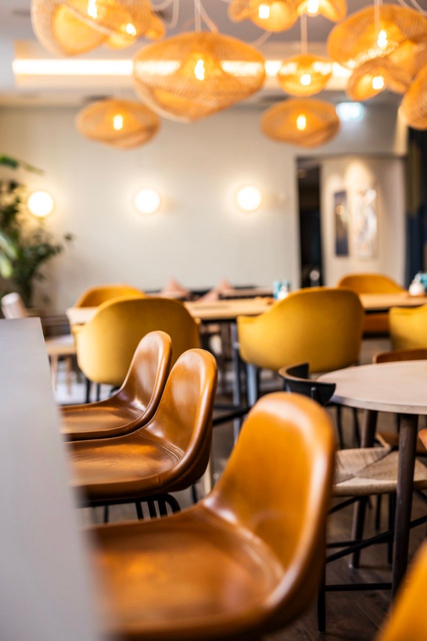 Moderne, einladende Hotelbar mit warmen Ledersesseln und sanfter Beleuchtung durch dekorative Hängelampen, ideal für entspannte Stunden und geselliges Beisammensein in stilvollem Ambiente.