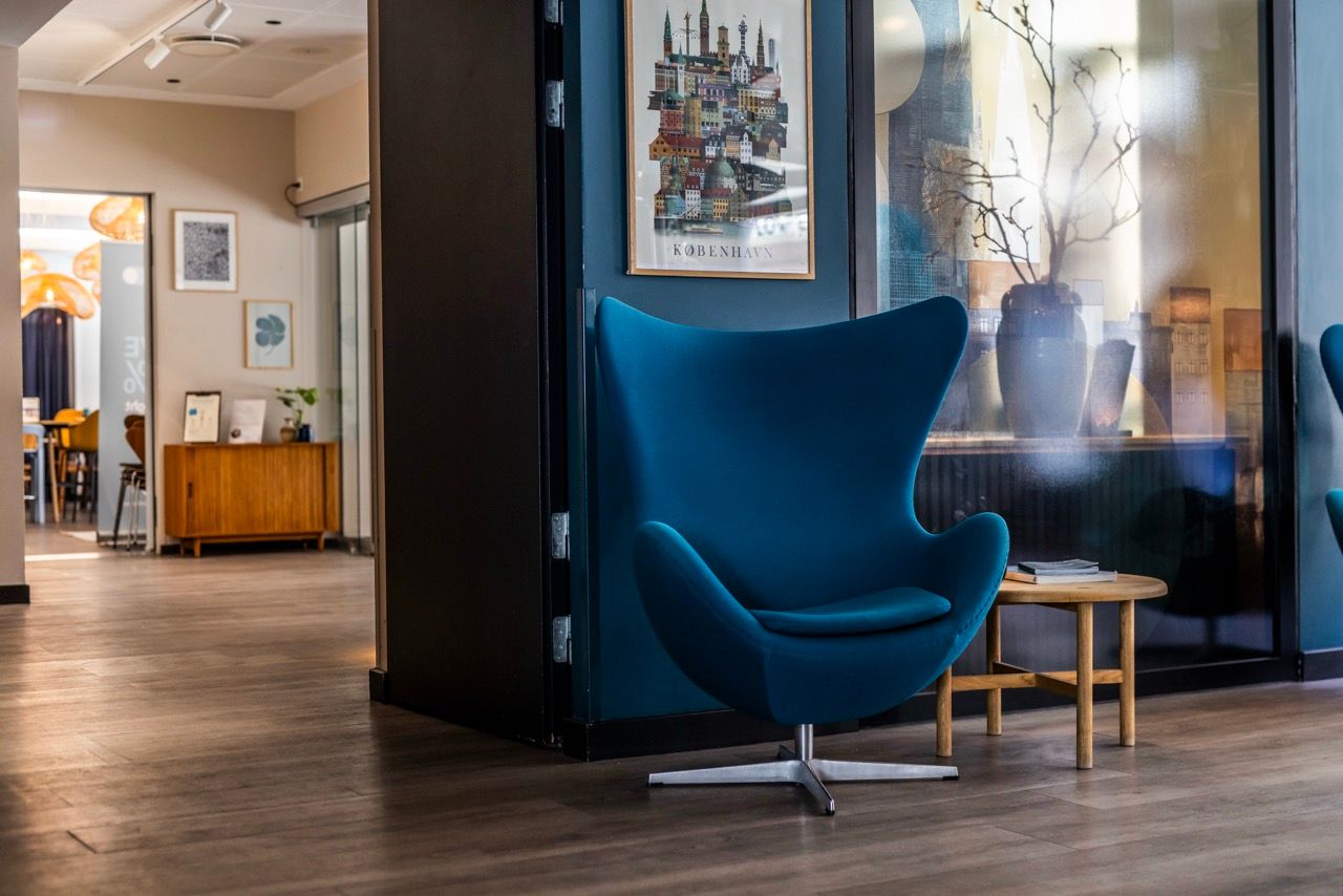 Moderner, komfortabler blauer Sessel neben einem kleinen Holztisch in stilvoll eingerichteter Hotel-Lounge mit warmem Ambiente und dekorativen Bildern an der Wand.