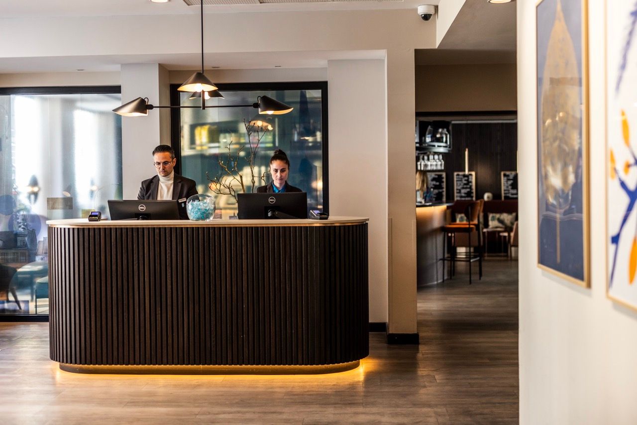 Hotelrezeption mit zwei Mitarbeitern am Empfangstresen, moderner und einladender Eingangsbereich, warme Beleuchtung, gepflegte Atmosphäre für einen professionellen Check-in.