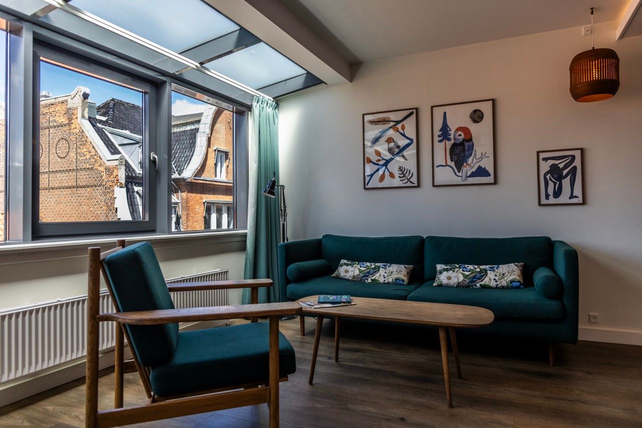 Helles Wohnzimmer mit großen Fenstern und Dachfenster, dunkelgrünem Sofa, bequemen Sesseln und moderner Wanddekoration, das einen entspannten und stilvollen Rückzugsort bietet.