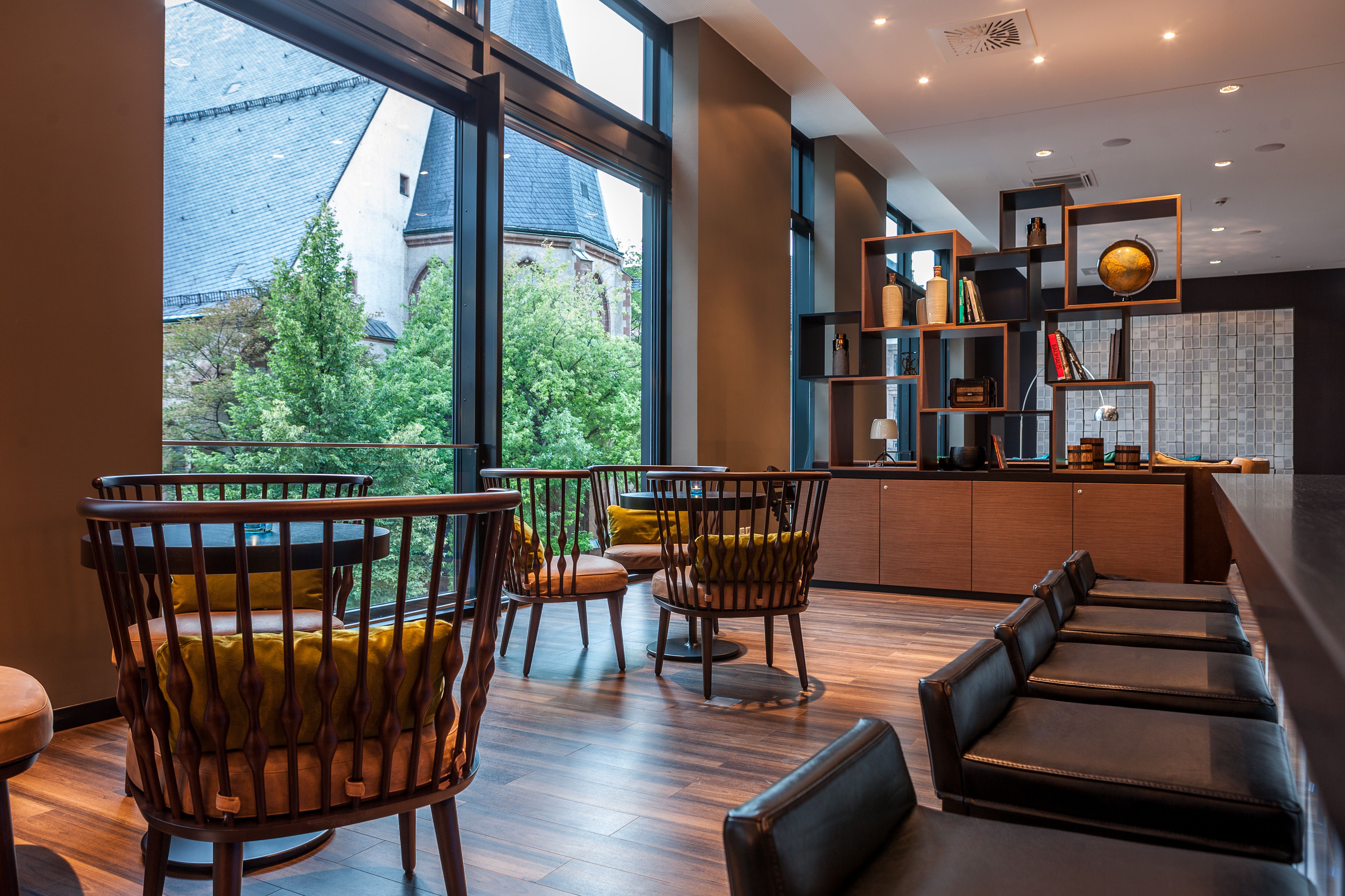 Hotel Leipzig Augustusplatz Motel One helle Lounge mit Sesseln, Stühlen, offenem Regal und bodentiefem Fenster