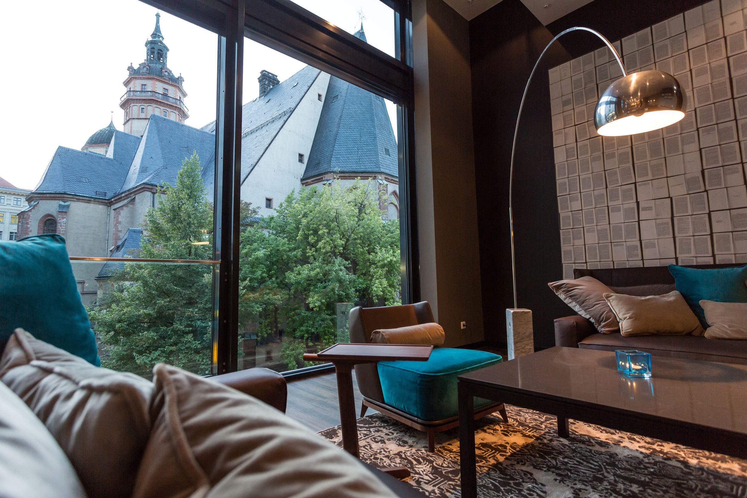 Hotel Leipzig Augustusplatz Motel One Blick über die Couch durch bodentiefes Fenster auf Kirche