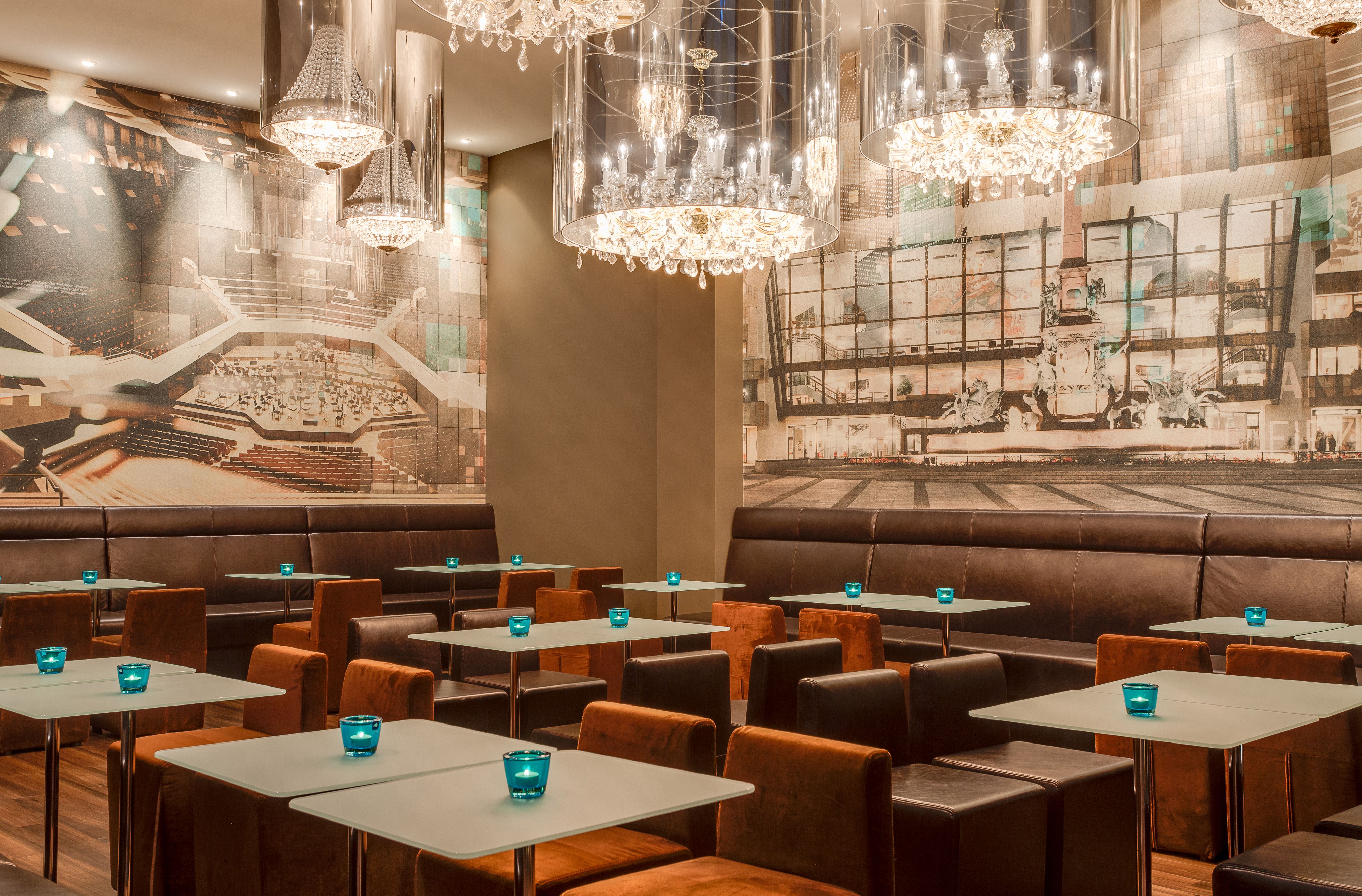 Hotel Leipzig Augustusplatz Motel One großer Raum mit Tischen und Stühlen sowie Gemälden an der Wand