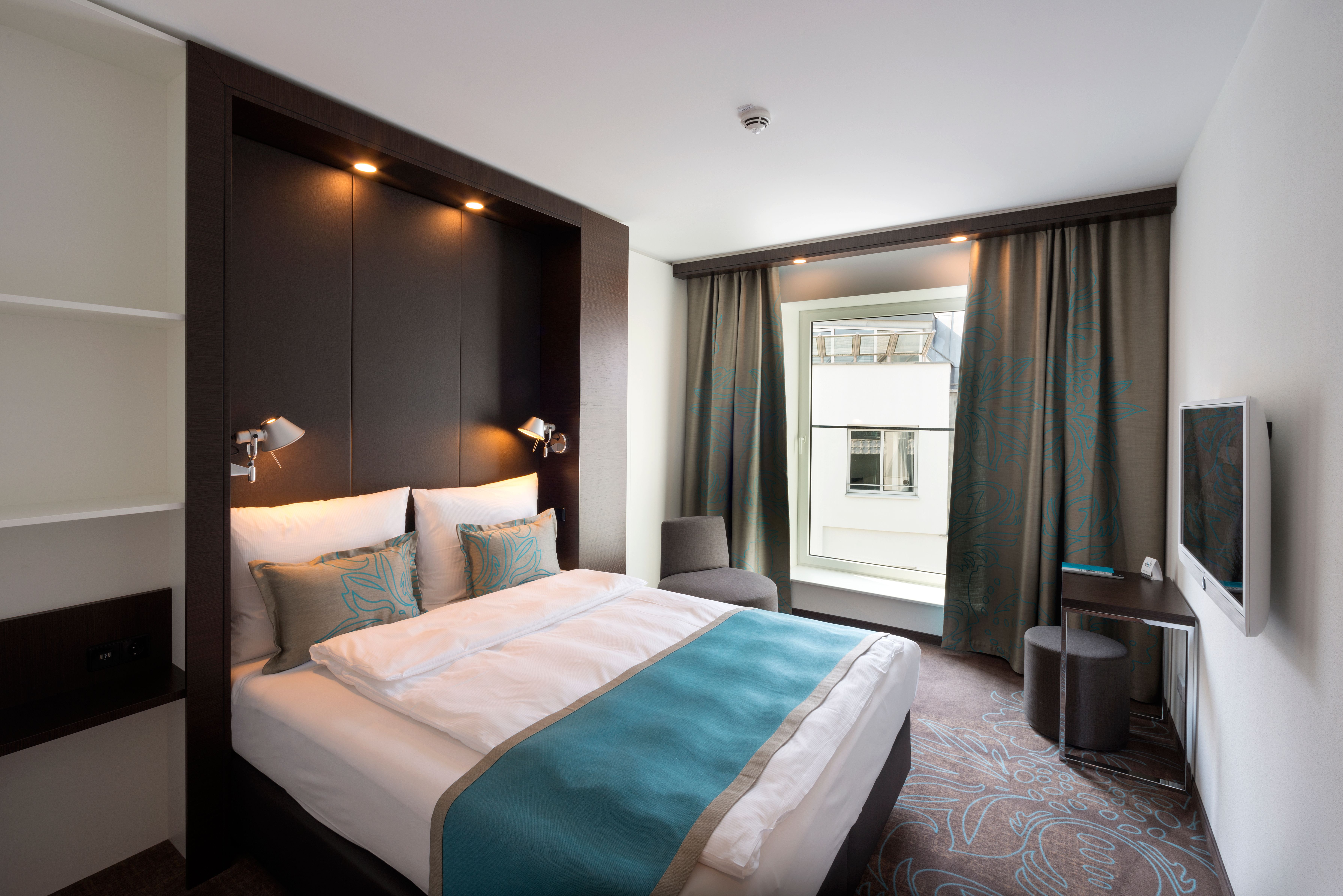 Hotel Leipzig Augustusplatz Motel One geräumiges Zimmer mit großem Bett sowie Sessel und Schreibtisch