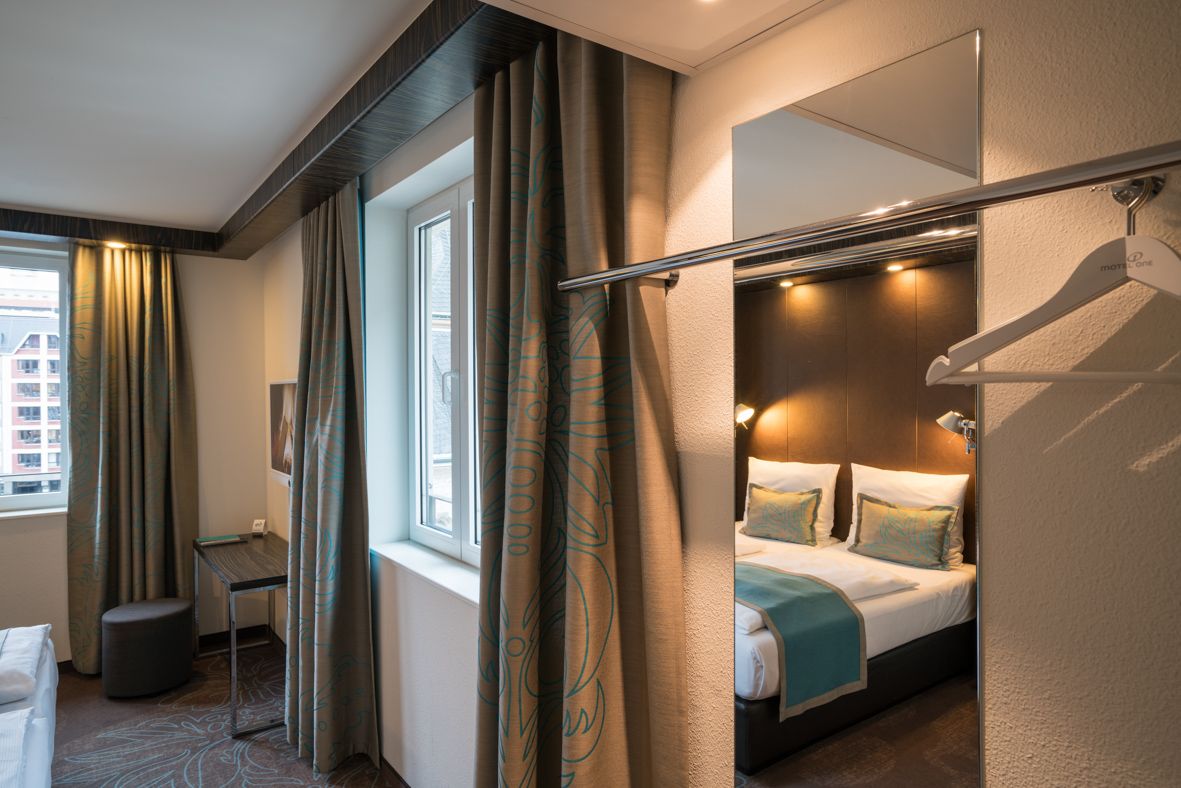 Designhotel Leipzig Nikolaikirche Motel One helles Zimmer mit großem Spiegel, durch den ein Doppelbett zu sehen ist