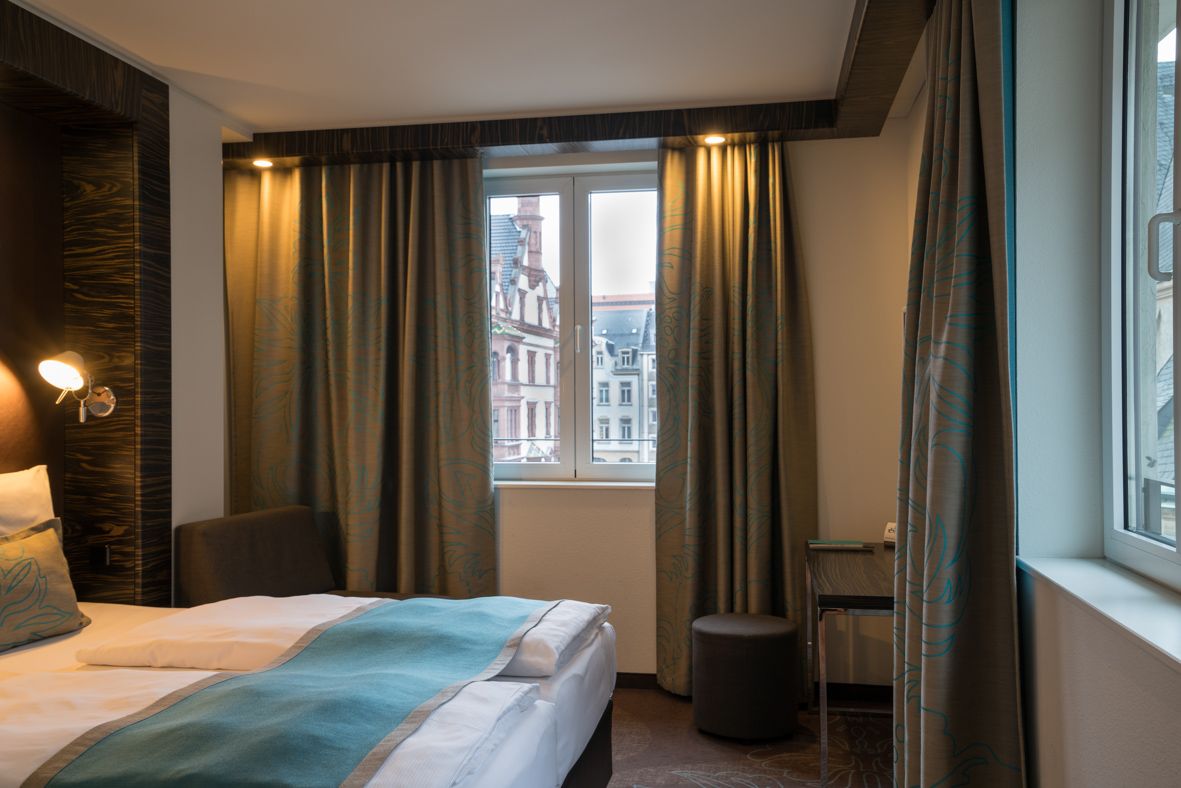 Designhotel Leipzig Nikolaikirche Motel One Eckzimmer mit großem Bett sowie Schreibtisch, Sessel und Hocker