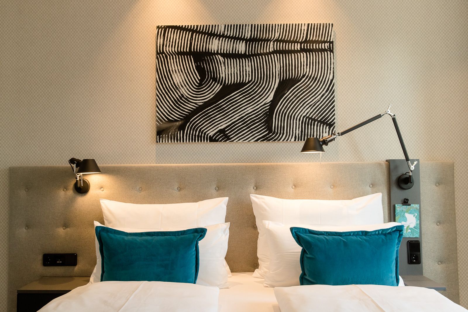 Designhotel Linz Hauptplatz Motel One Blick auf Doppelbett mit Zierkissen sowie Bild in schwarz-weiß über dem Bett