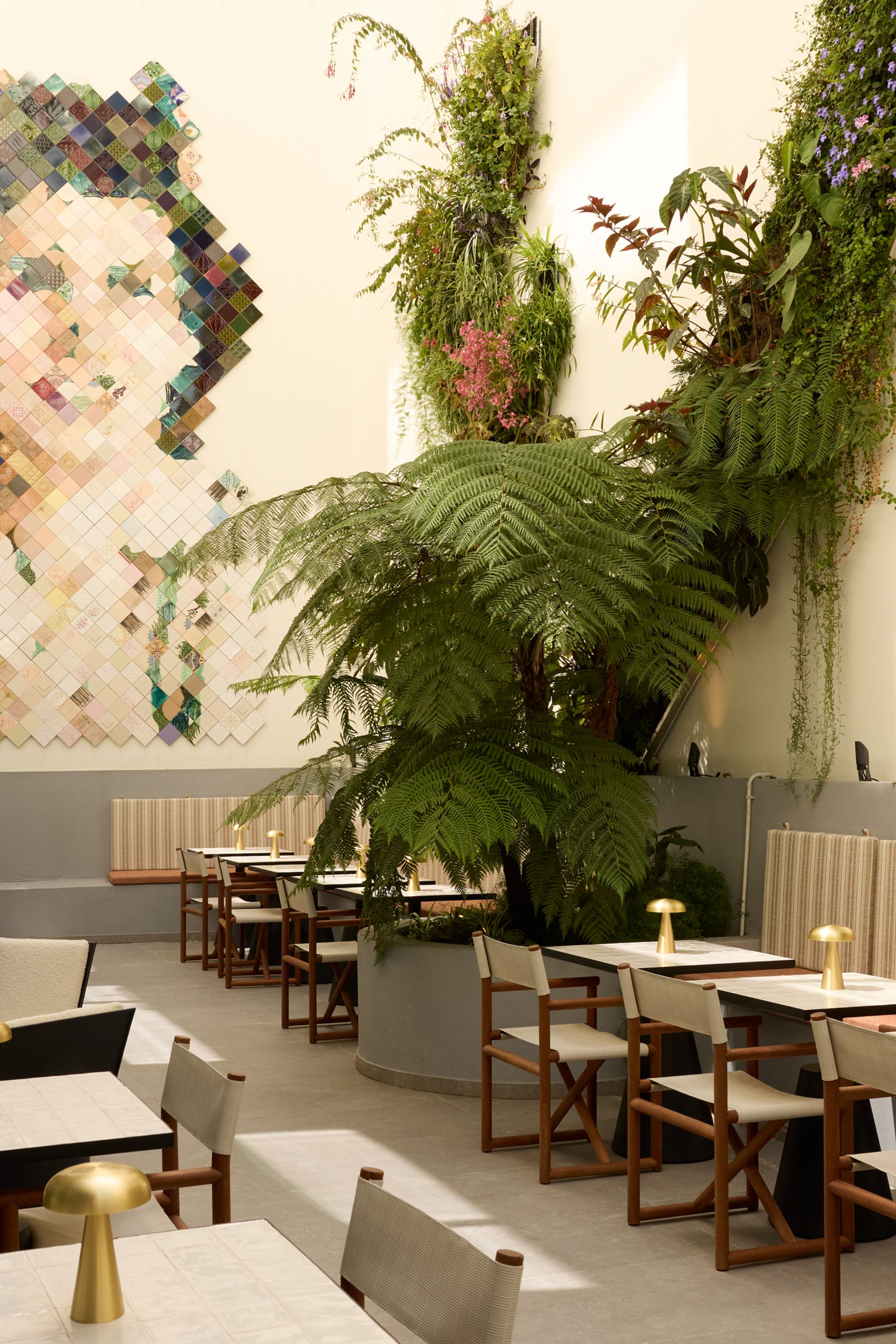 Heller, freundlicher Innenhof mit gemütlichen Sitzplätzen, grünen Pflanzen und einer großen Wandkunst, die ein Gesicht darstellt. Ideal für entspannte Mahlzeiten oder Gespräche in ruhiger Atmosphäre.