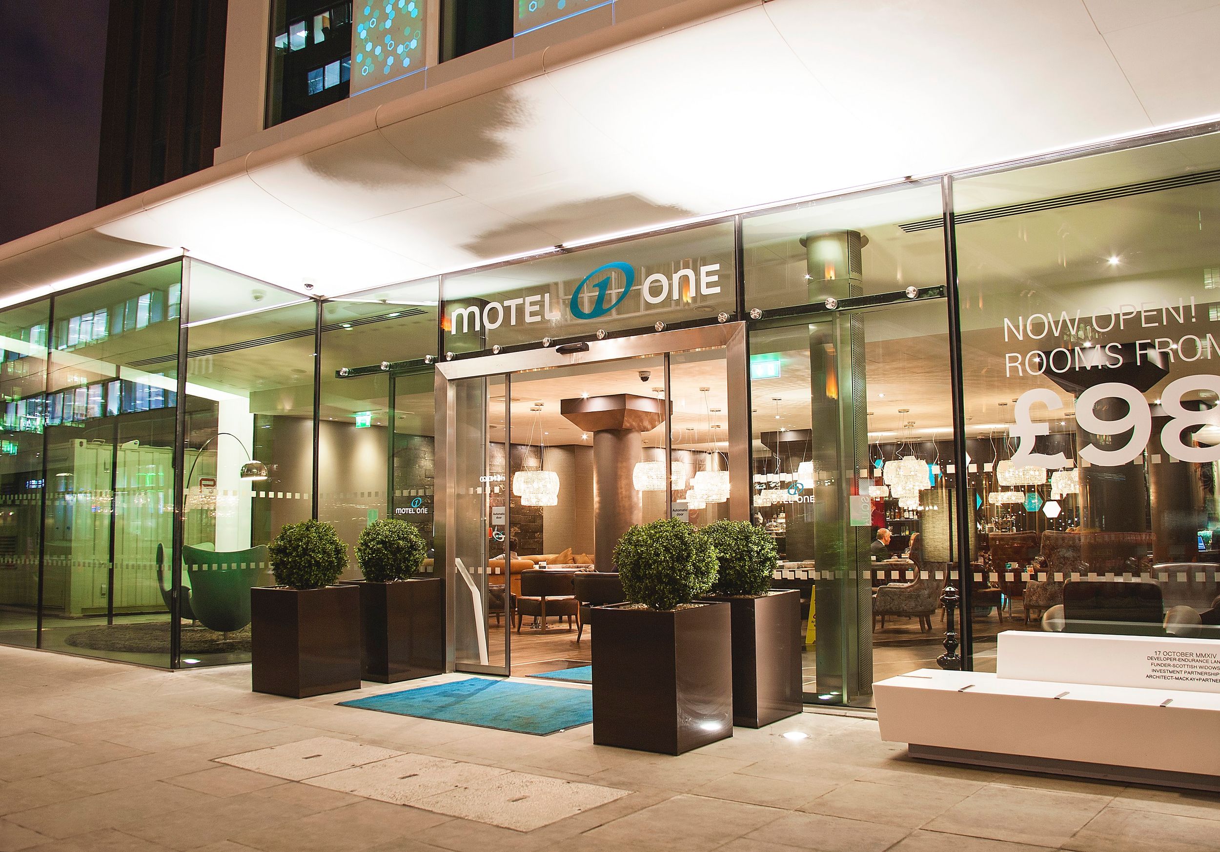 Hotel London Tower Hill Motel One Blick von außen auf den hell erleuchteten Eingangsbereich bei Abend