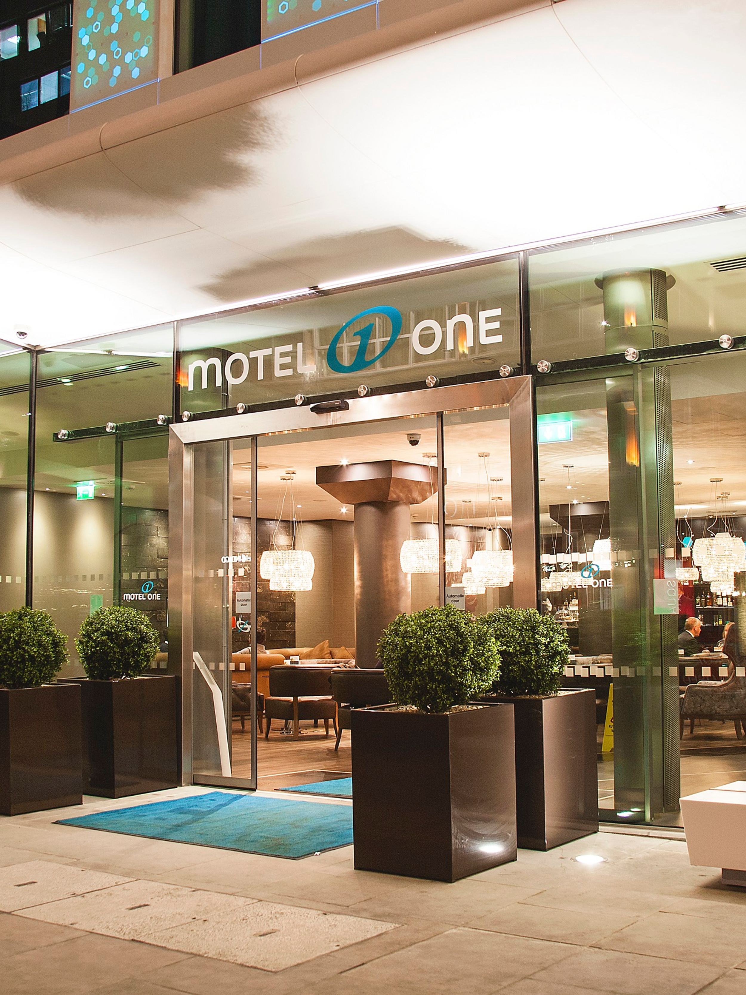 hotel London Tower Hill Motel One view from outside of the brightly lit entrance area at night