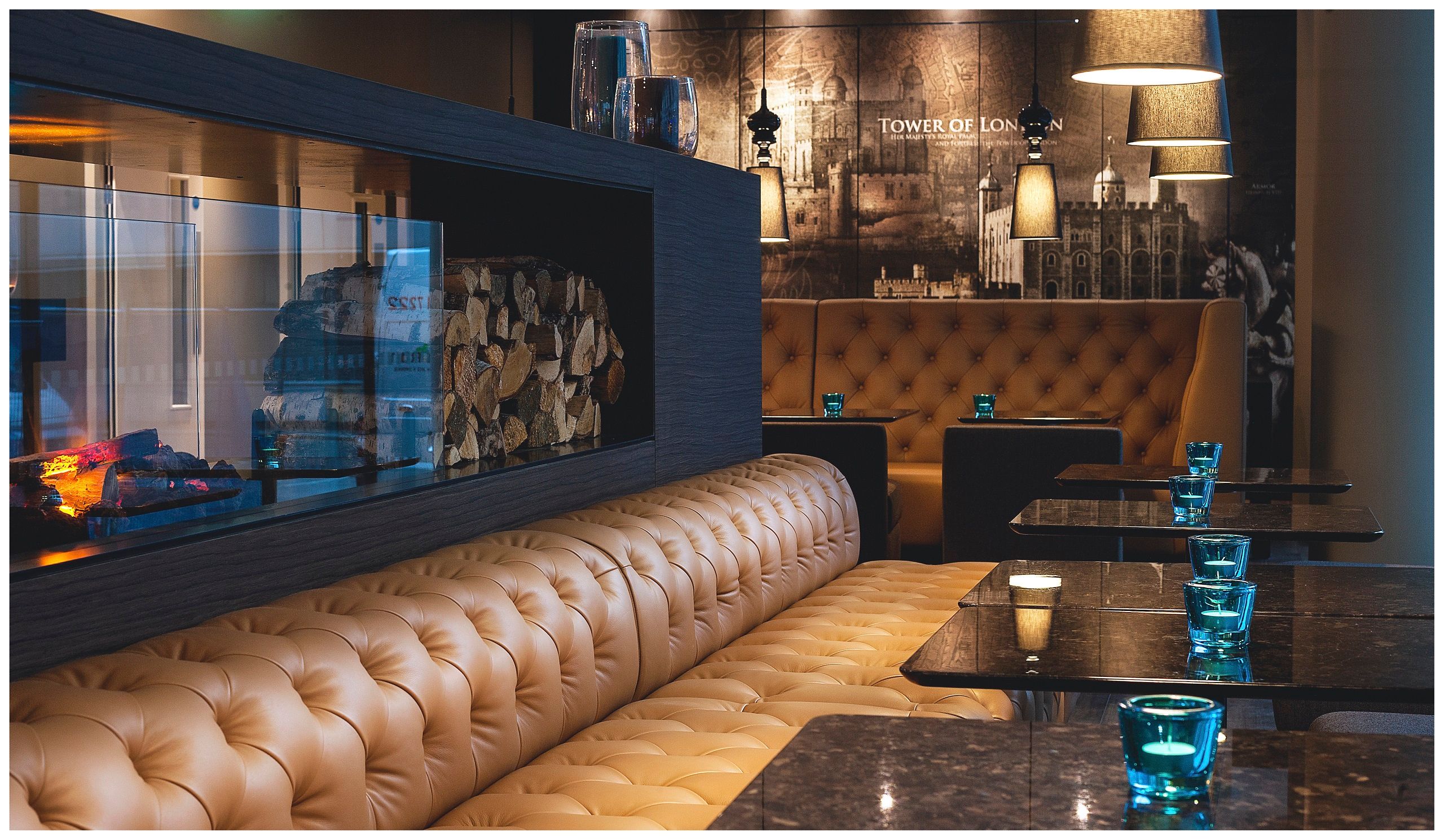 Hotel London Tower Hill Motel One Lounge mit langer Couch sowie Tischen und Kaminfeuer