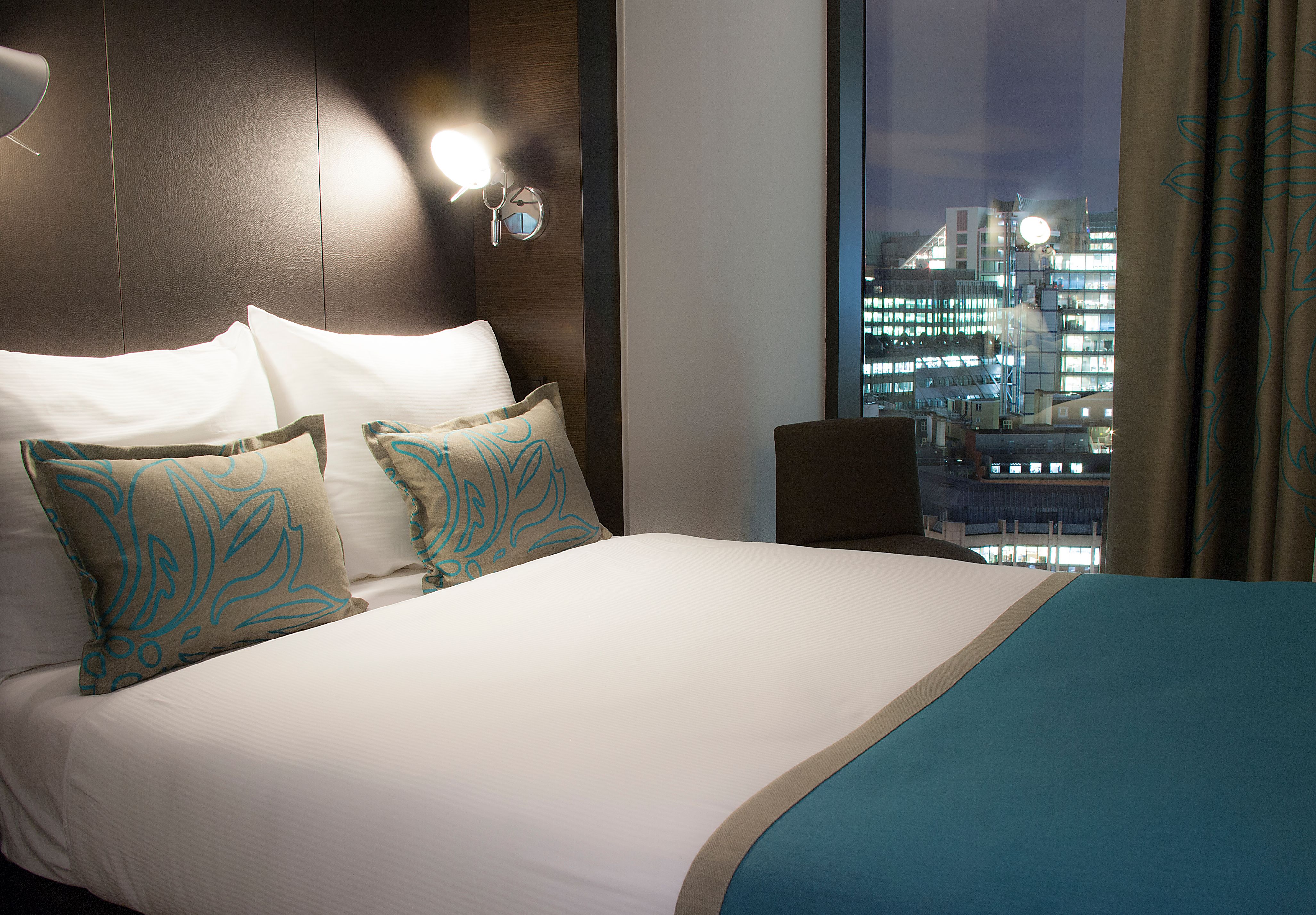 Hotel London Tower Hill Motel One Zimmer mit Doppelbett und Sessel vor dem Fenster bei Abend