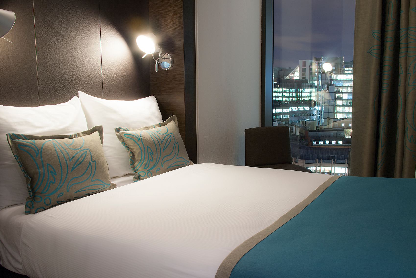 Hotel London Tower Hill Motel One Zimmer mit Doppelbett und Sessel vor dem Fenster bei Abend