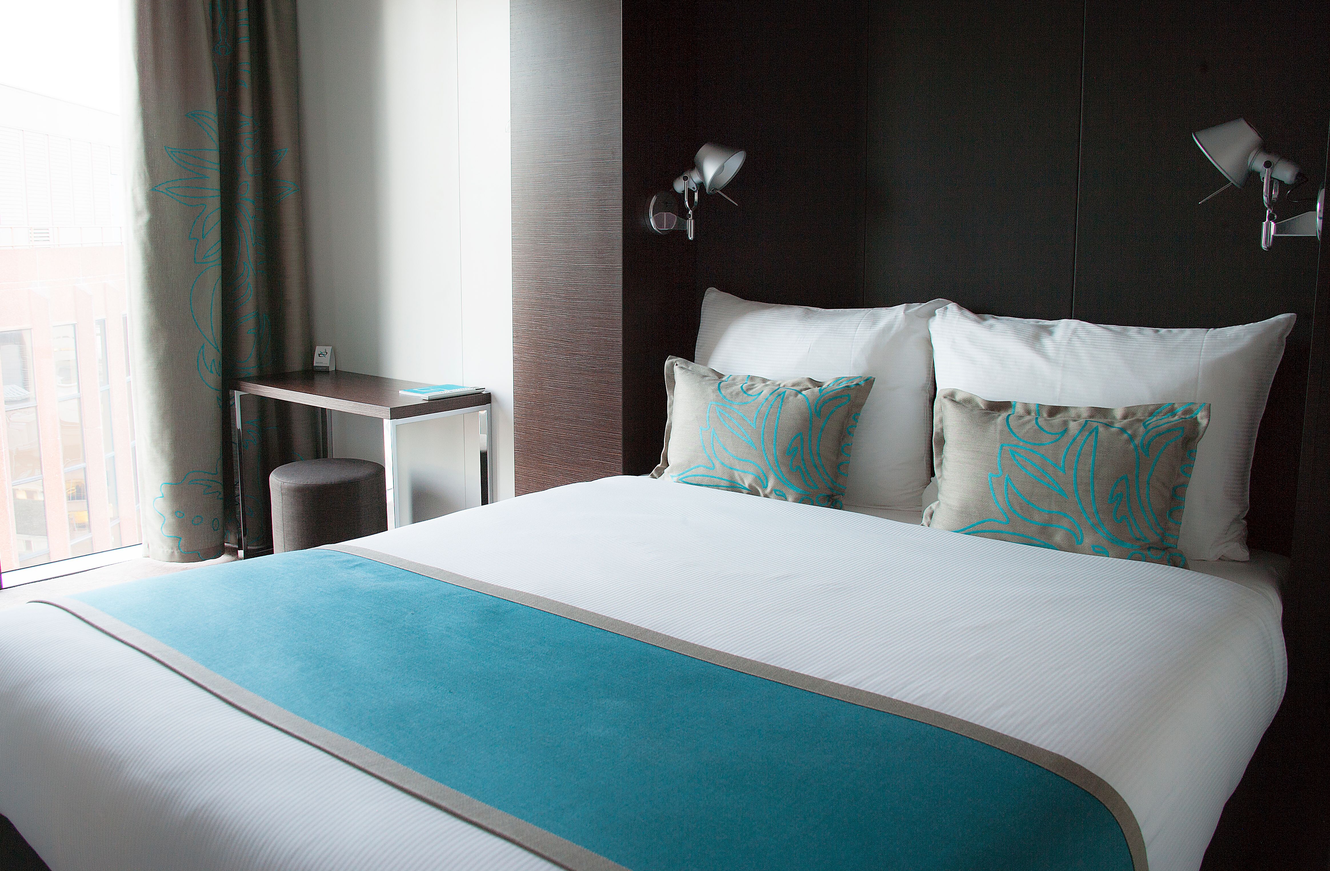 Hotel London Tower Hill Motel One Doppelbett mit Zierkissen sowie kleiner Tisch mit Hocker neben dem Bett