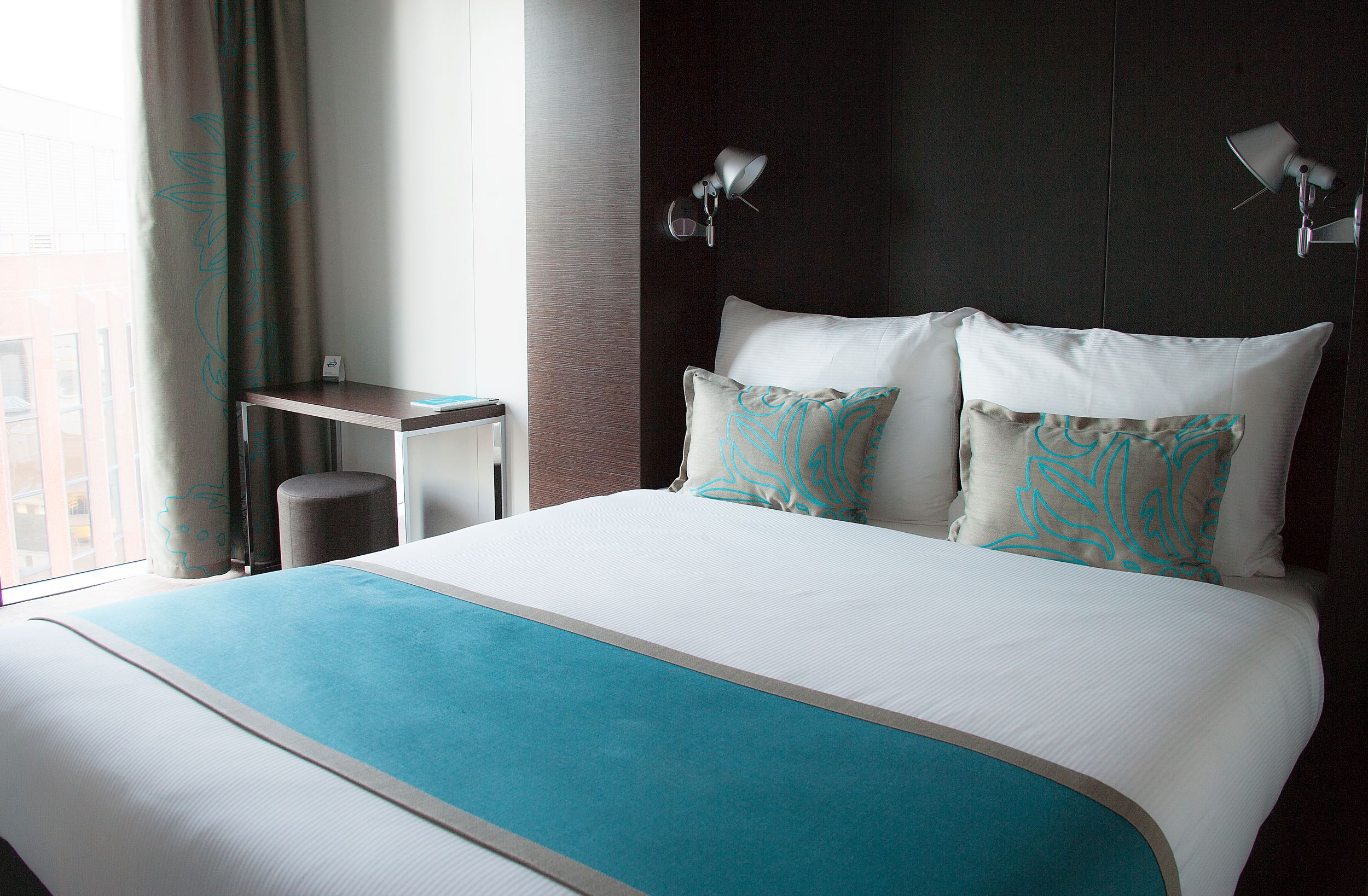 Hotel London Tower Hill Motel One double bed with decorative cushions and small table with stool next to the bed